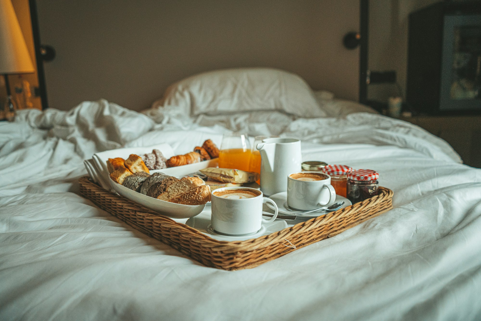 Breakfast tray with pastries, coffee and orange juice on an unmade bed