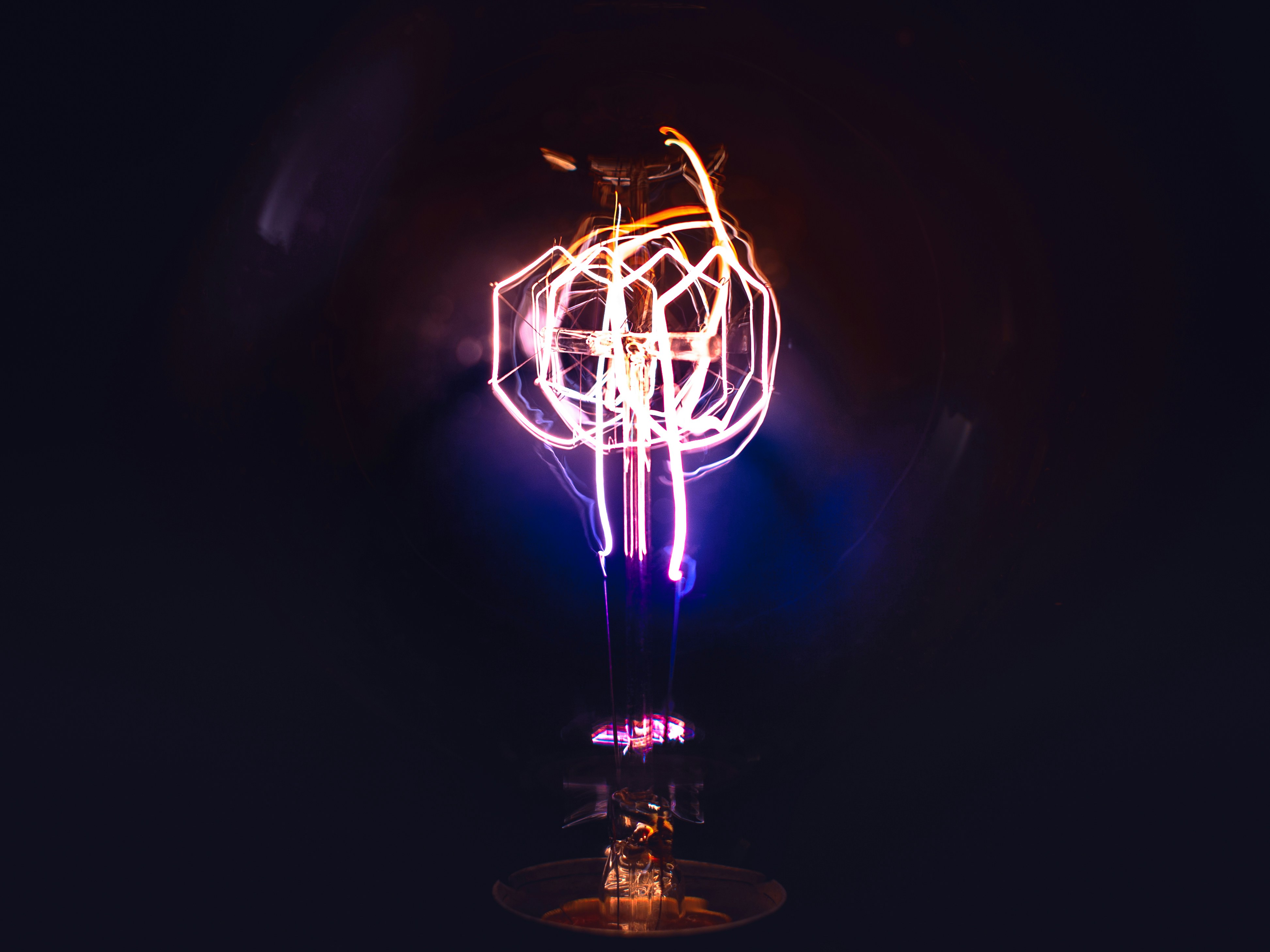 A lit fluroescent lightbulb with pink, orange purple colours lit up aganst a black background.