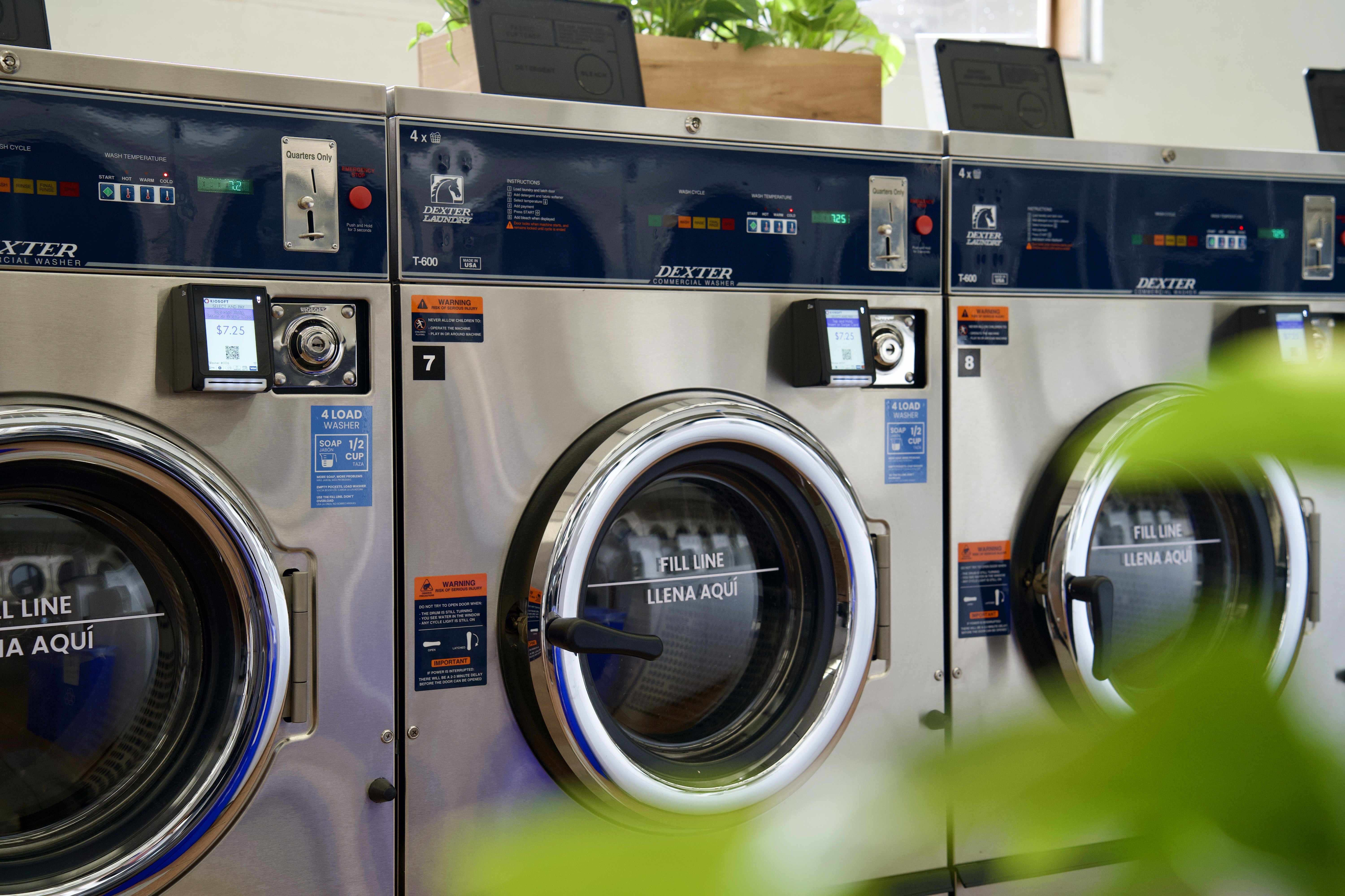 Interior of a laundromat with several washing machines lined up against blue walls and bright lighting.
