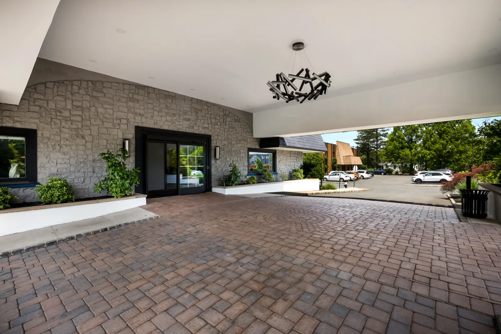 Stone building entrance with covered paved driveway and modern chandelier.
