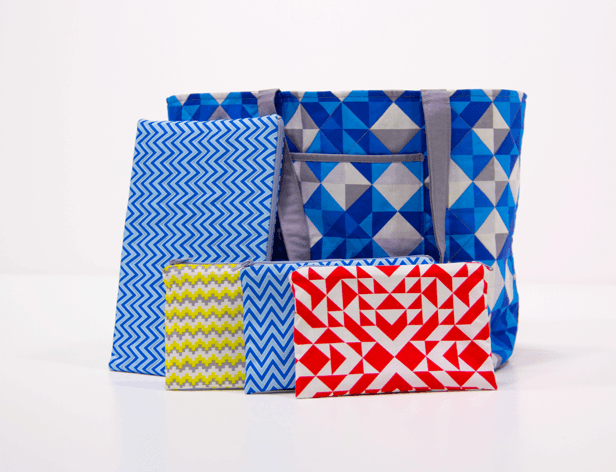 Four gift bags are arranged on a white surface against a white background. The largest bag is blue with a geometric pattern of blue and gray triangles. To its left is a blue chevron-patterned bag. To its right is a smaller blue and white chevron bag. Below the blue chevron bag is a yellow and white chevron-patterned bag. To the right of the blue chevron bag is a red and white geometric-patterned bag.