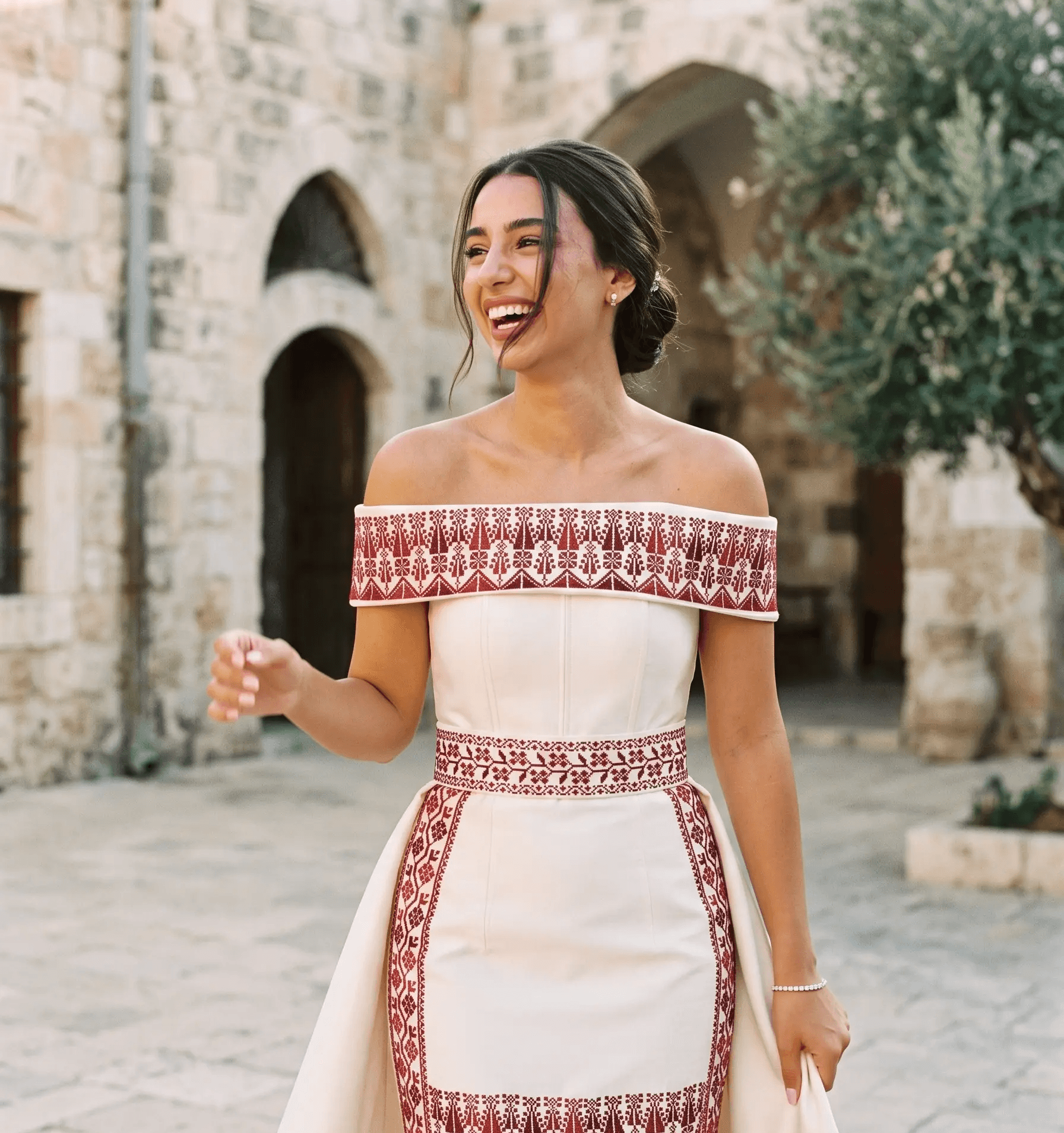 Bride laughing in a Palestinian tatreez-embroidered gown in an old stone courtyard