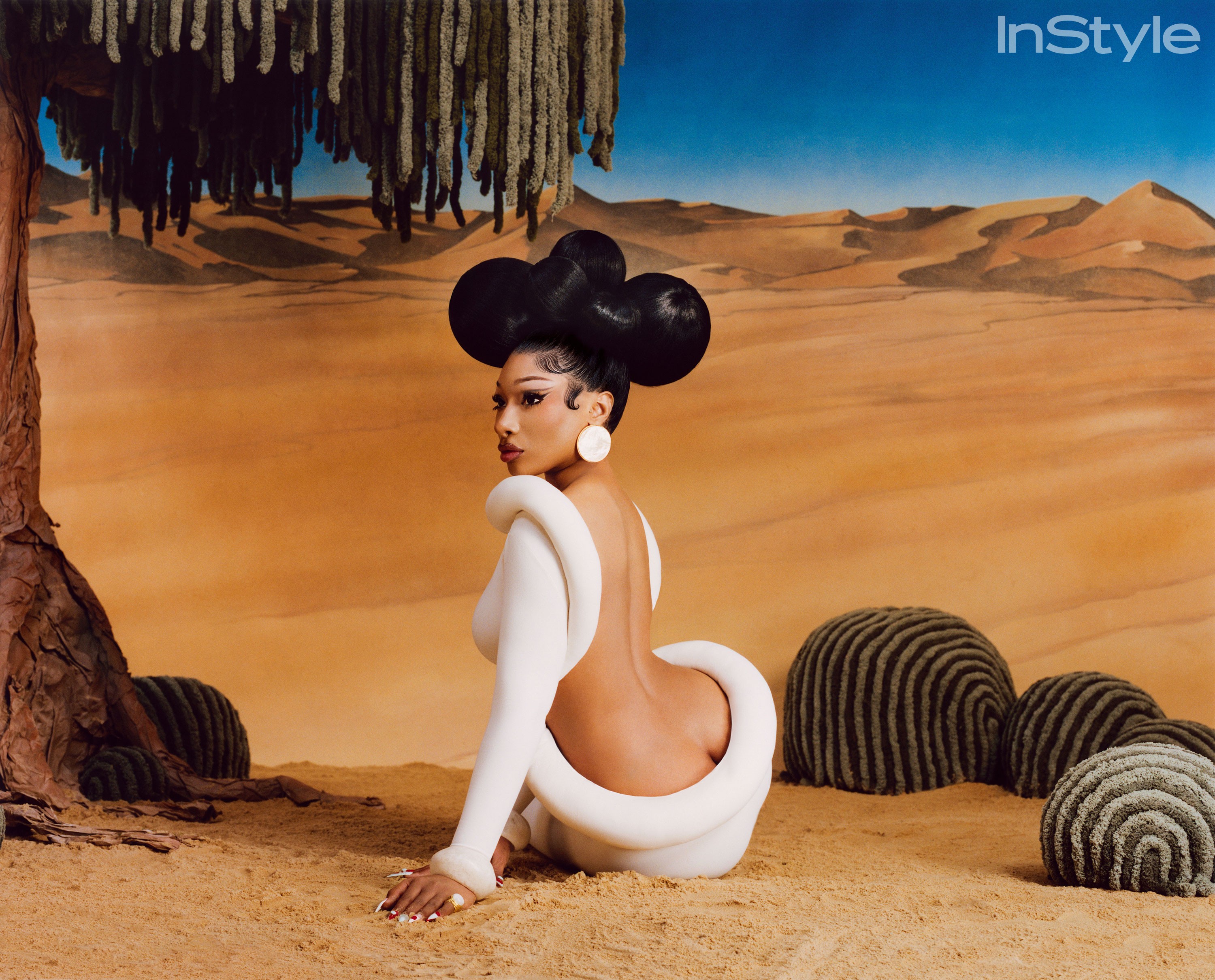 Megan Thee Stallion seated in a white backless dress on the desert set