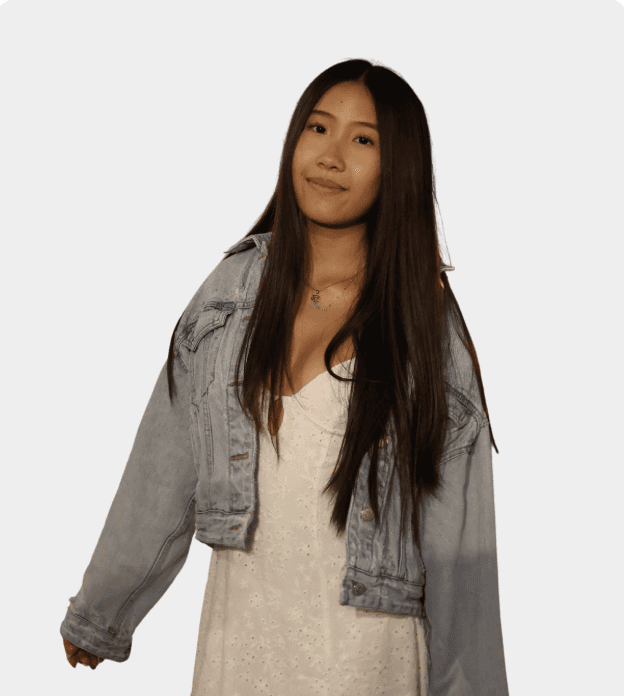 A smiling person with curly hair sits at a desk with computers in a stylish, well-lit office setting.