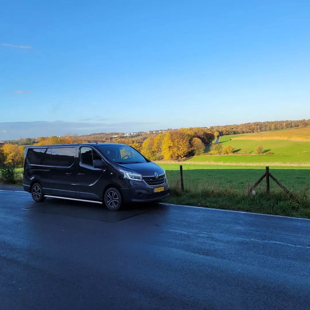 Zwarte bestelbus van Van Ede Koeriers geparkeerd langs een landelijke weg met uitzicht over de velden.