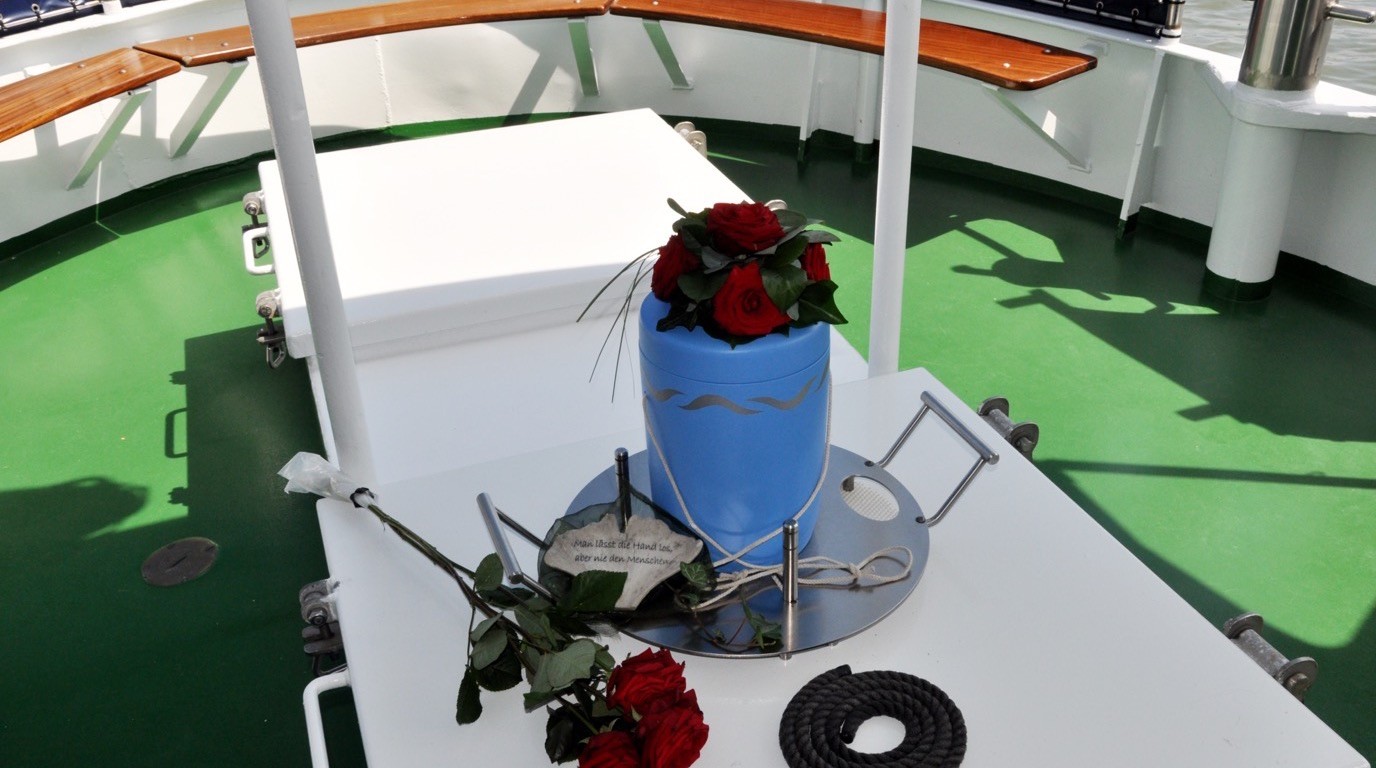 Blaue Seeurne mit roten Rosen auf dem Deck eines Bestattungsschiffs vor der Beisetzung