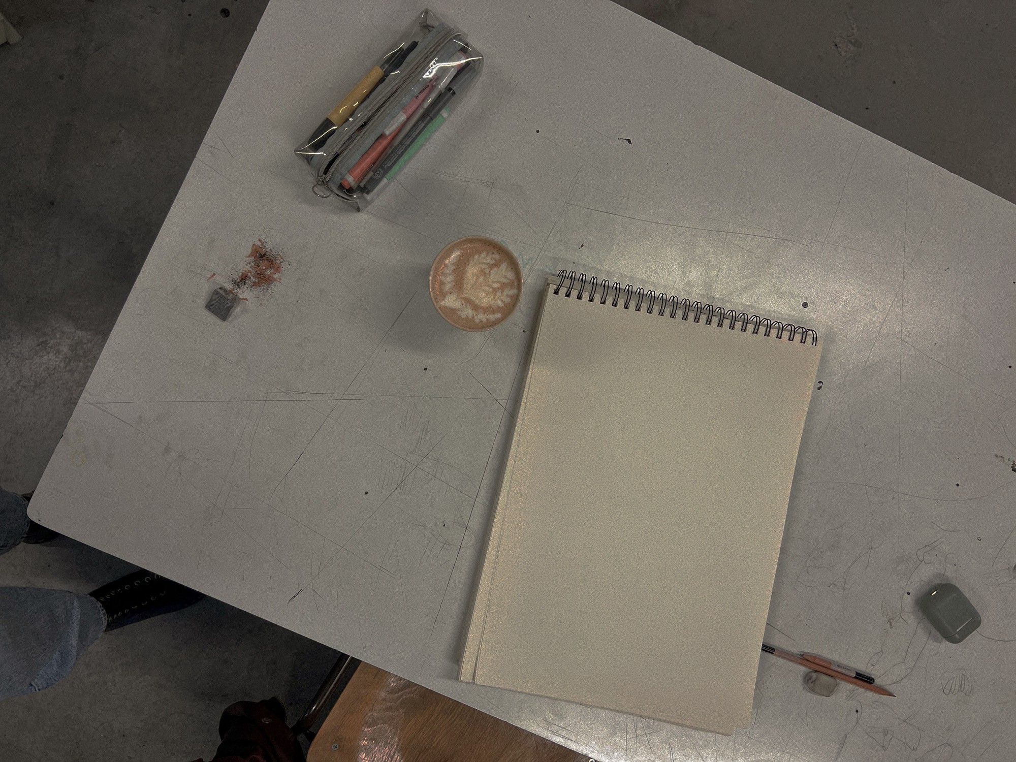 Bovenaanzicht van een werktafel met een schetsboek, grafietpotlood en een kop koffie in een ontwerpstudio.