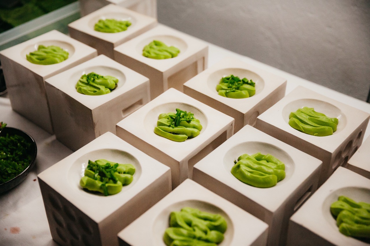 A woman in an orange sweater, wearing glasses, focused on coding at a computer screen.