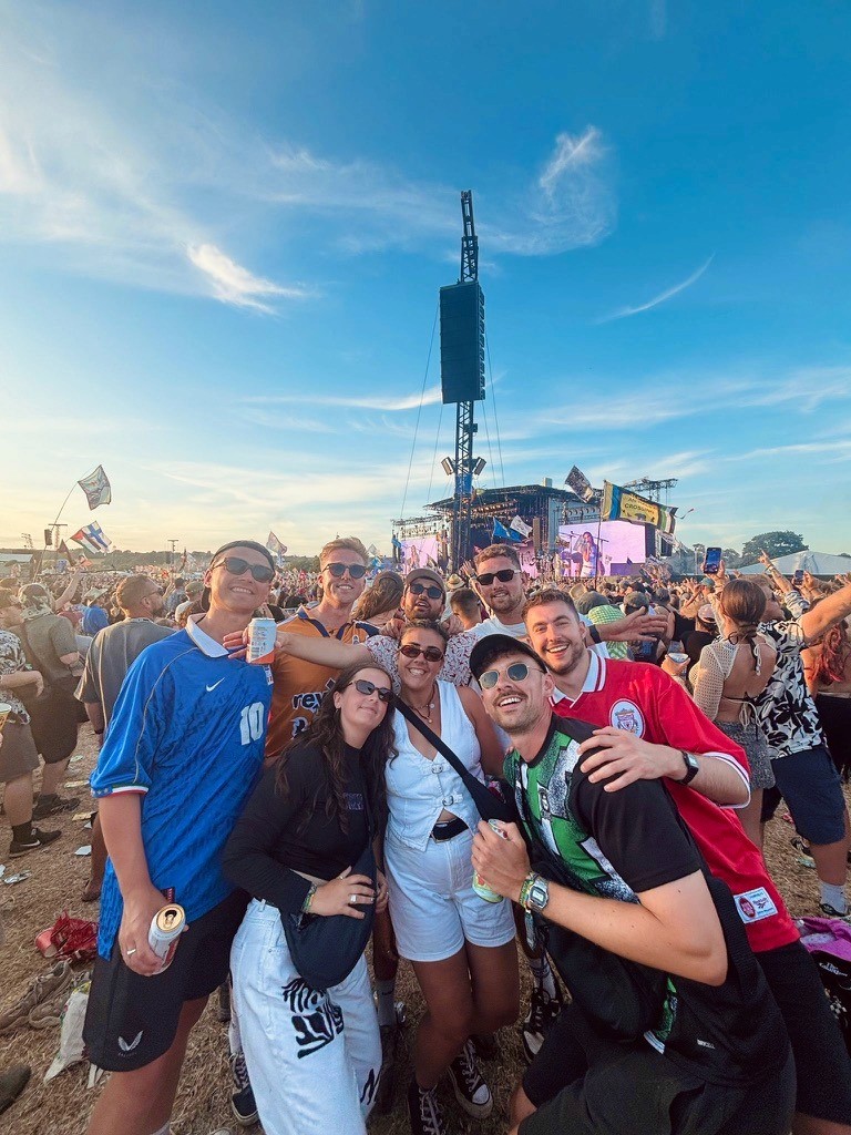 Person wearing a blue puffer jacket and red backpack standing in front of a light blue building on a city street.