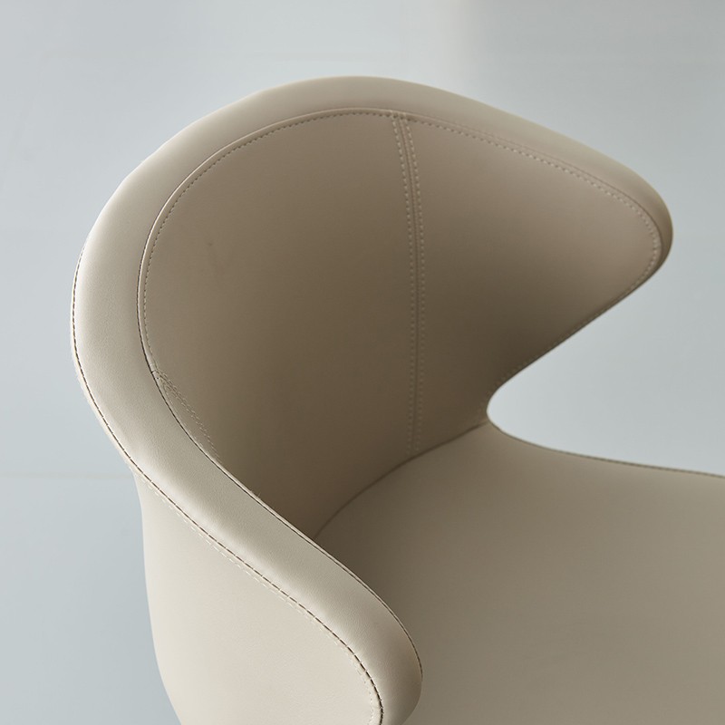 Detailed close-up of a light beige leather office chair showing the elegant wing-like curves of the ergonomic backrest and precision perimeter stitching.