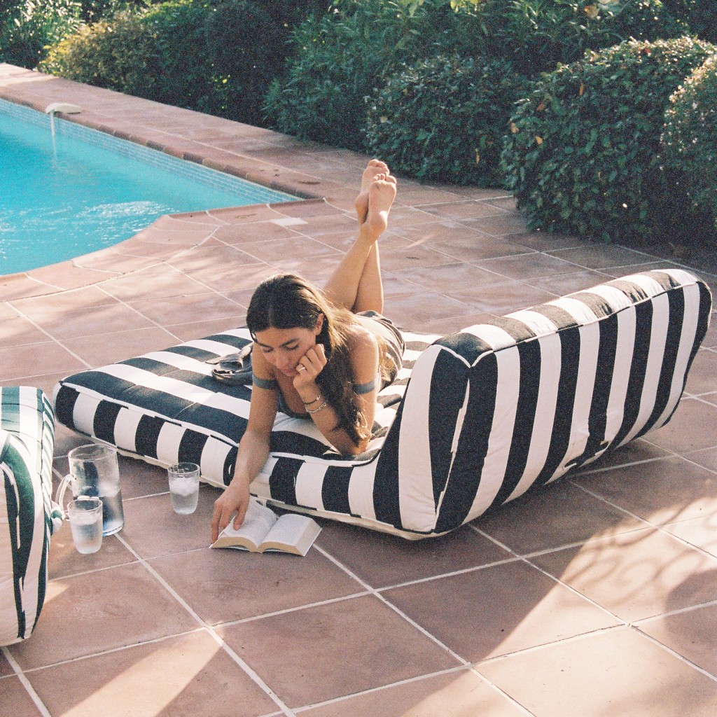 Woman lounging poolside on a luxury black-and-white striped pool float at a Mediterranean villa