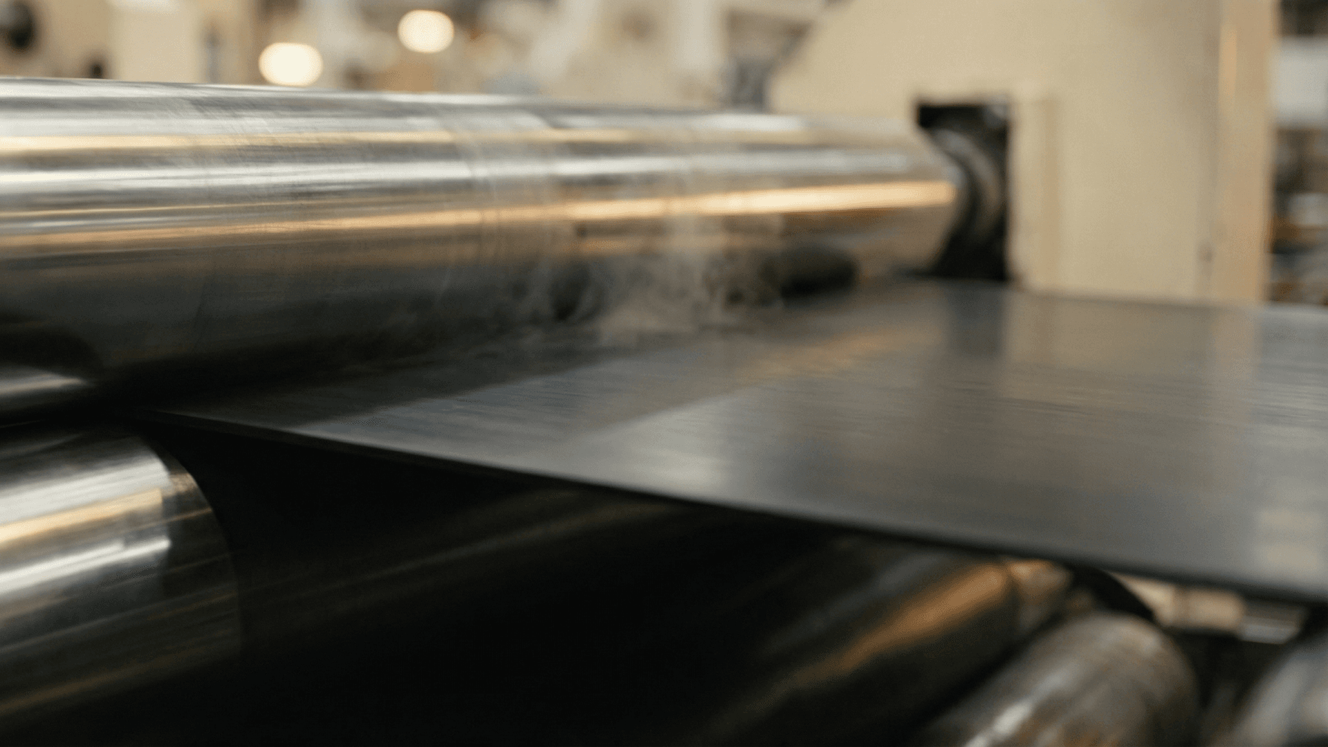 Steel rollers pressing a sheet of black rubber on a tire production line