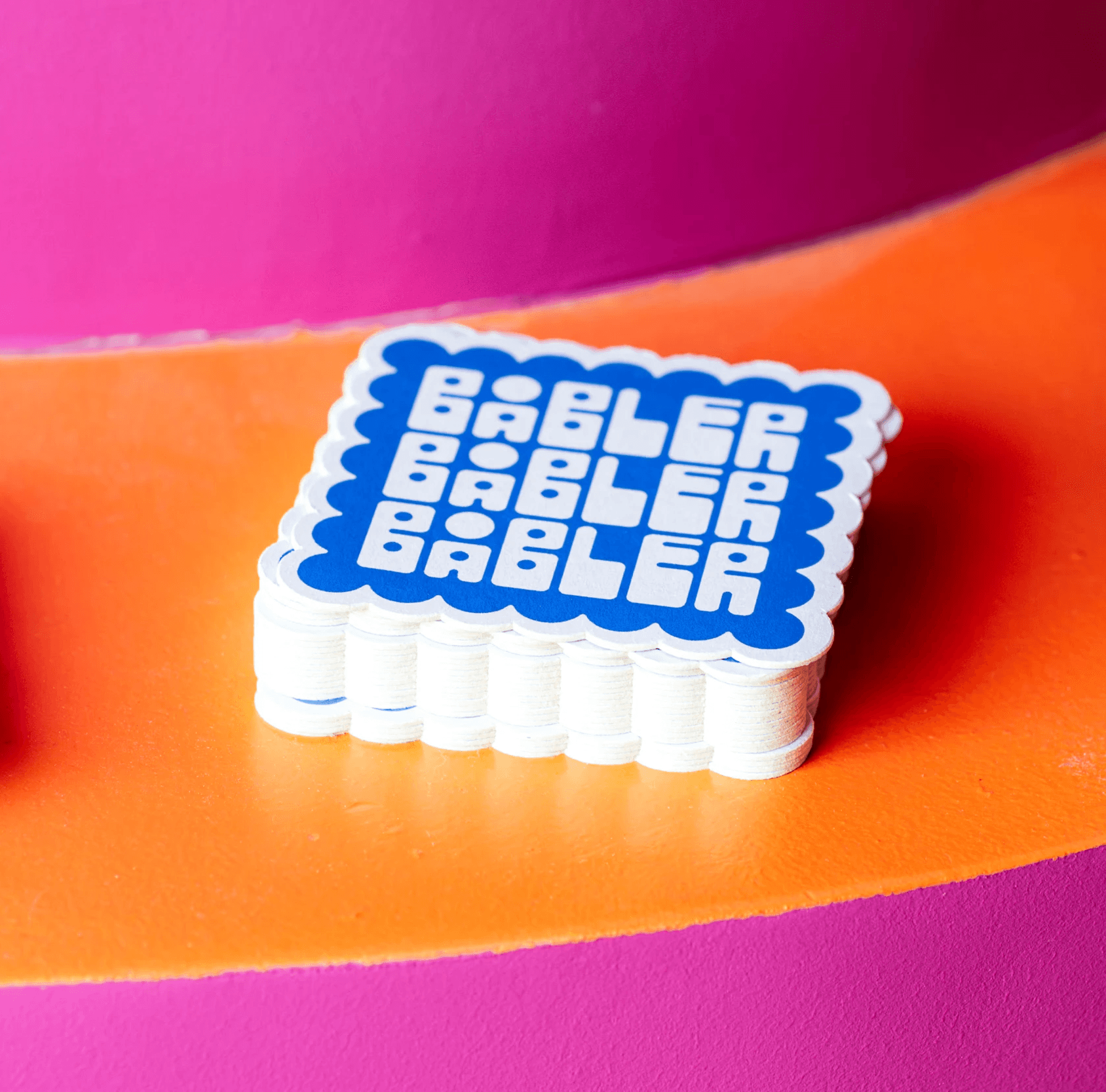 Coaster designs for Båbler wine bar laying in a stack on a orange and pink table.