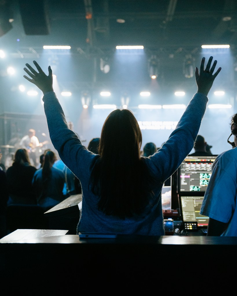 A lively concert scene with bright lights illuminating a band on stage and a cheering audience in the foreground.