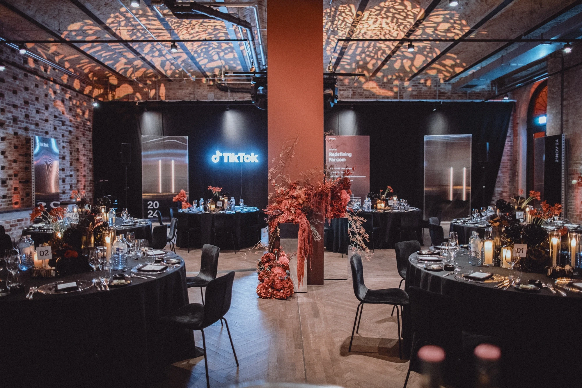 Gala dinner room with black round tables, red flower columns, TikTok logo and patterned light ceiling.