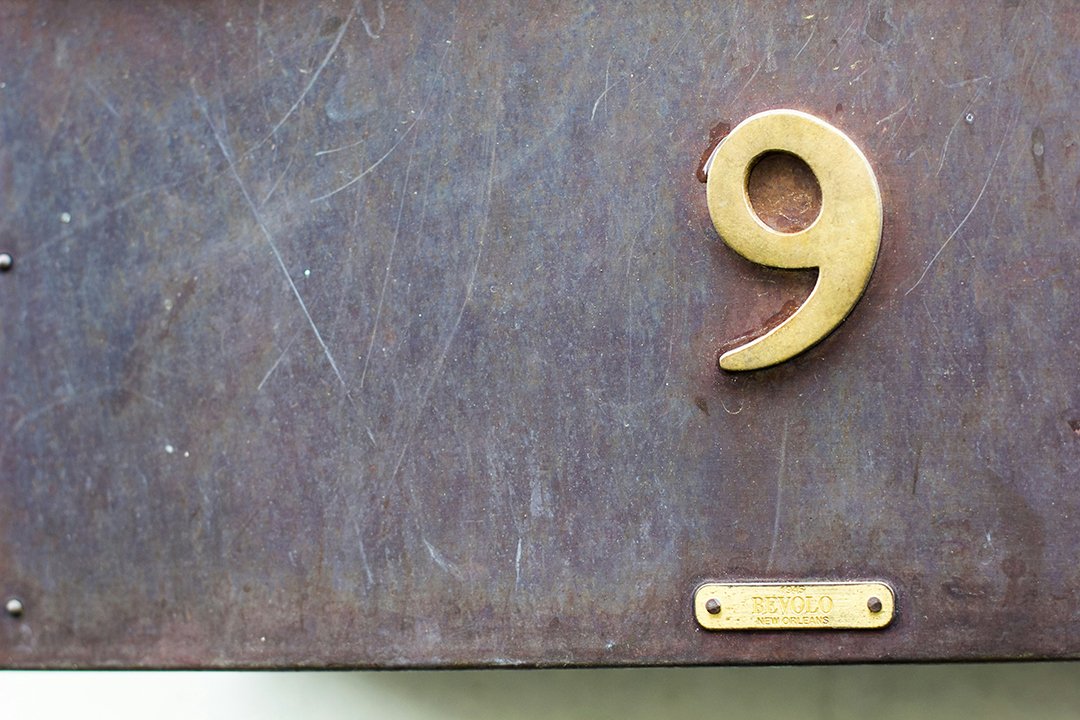 A brass number nine mounted on a weathered grey panel