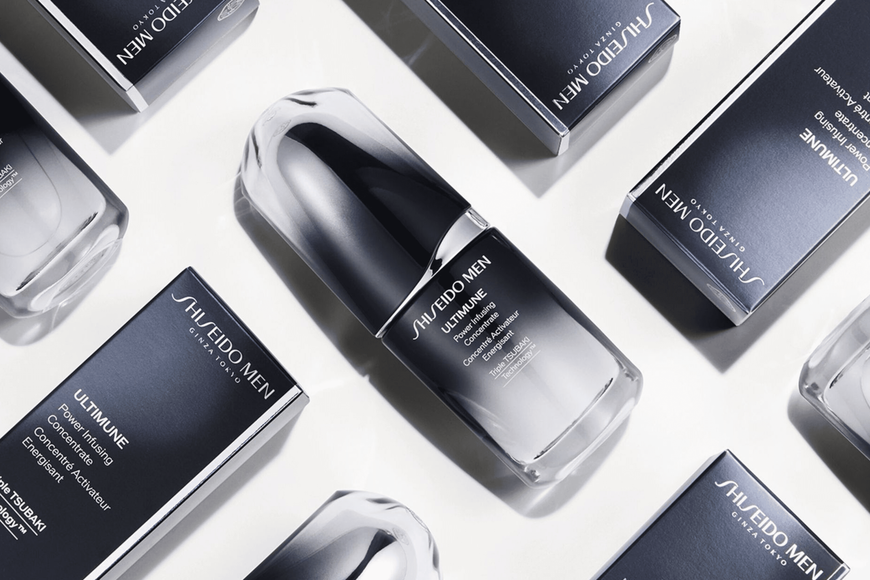 A collection of sleek, dark beauty product bottles and their packaging arranged artistically on a light background.