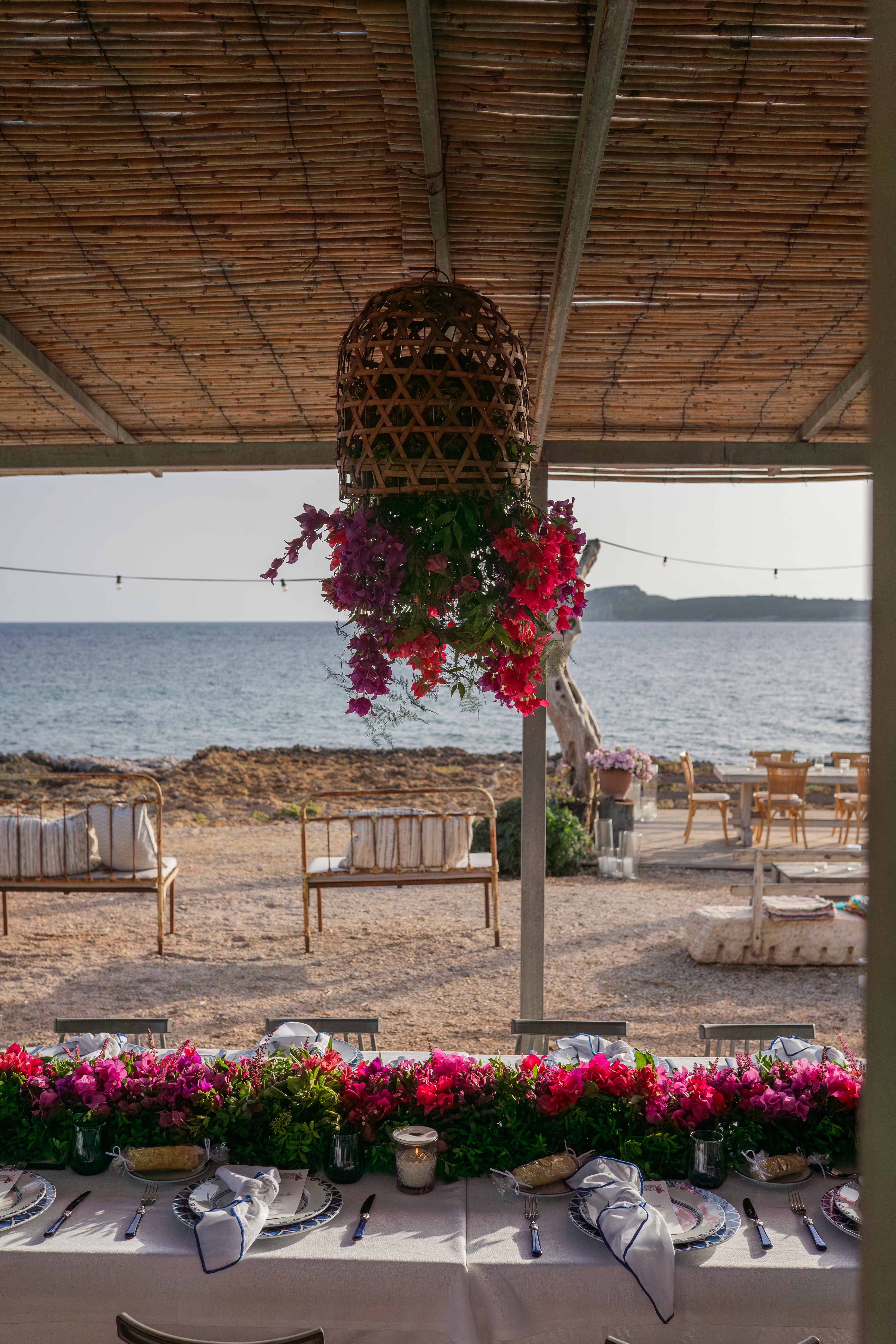 Ρουστίκ στολισμός τραπεζιού γάμου δίπλα στη θάλασσα με κρεμαστή ανθοσύνθεση από φούξια βουκαμβίλια