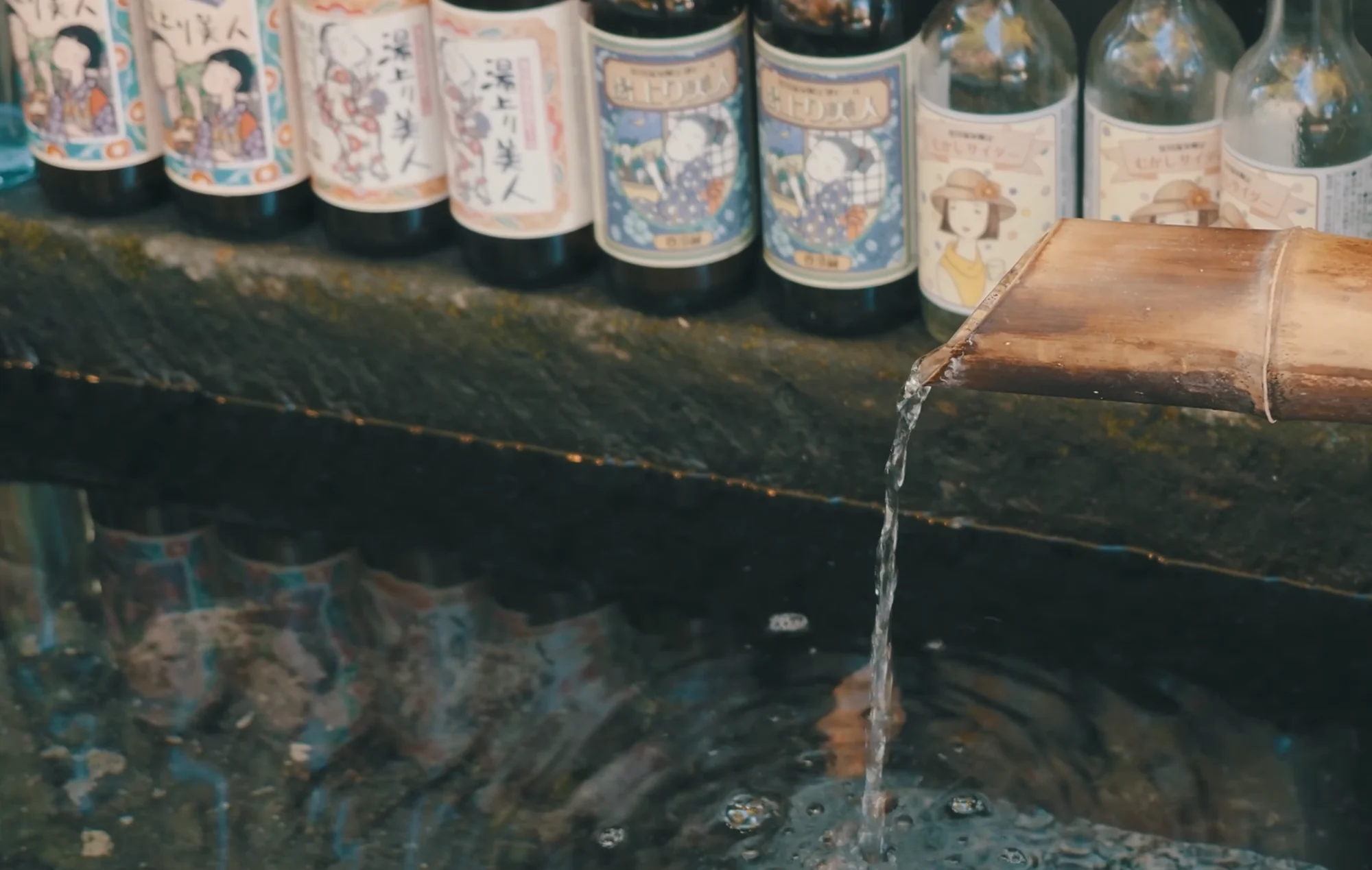 Bottled local drinks with illustrated labels cooling in a channel of running spring water
