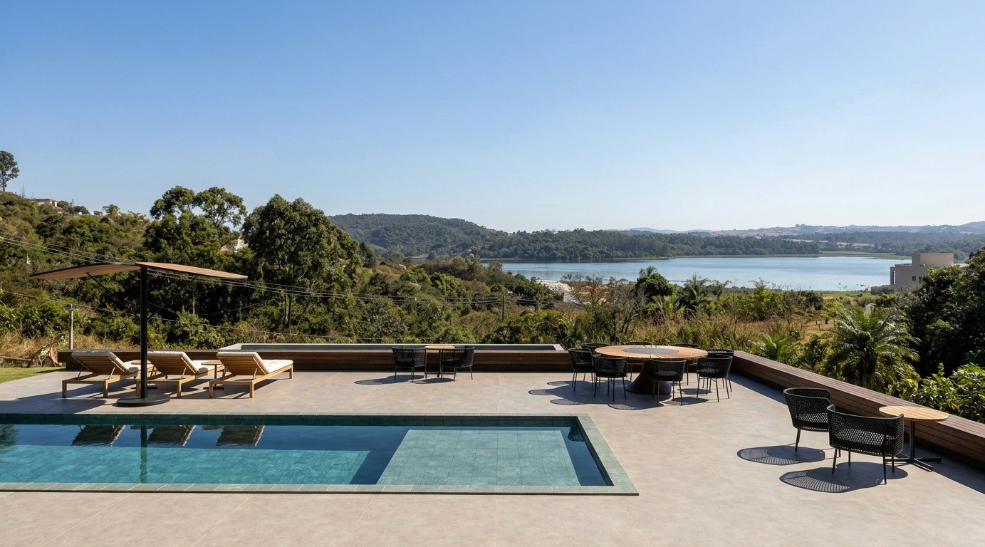 Terraço com piscina, espreguiçadeiras e mesa ao ar livre. Ao fundo, a encosta arborizada e a represa que não estavam no modelo 3D.
