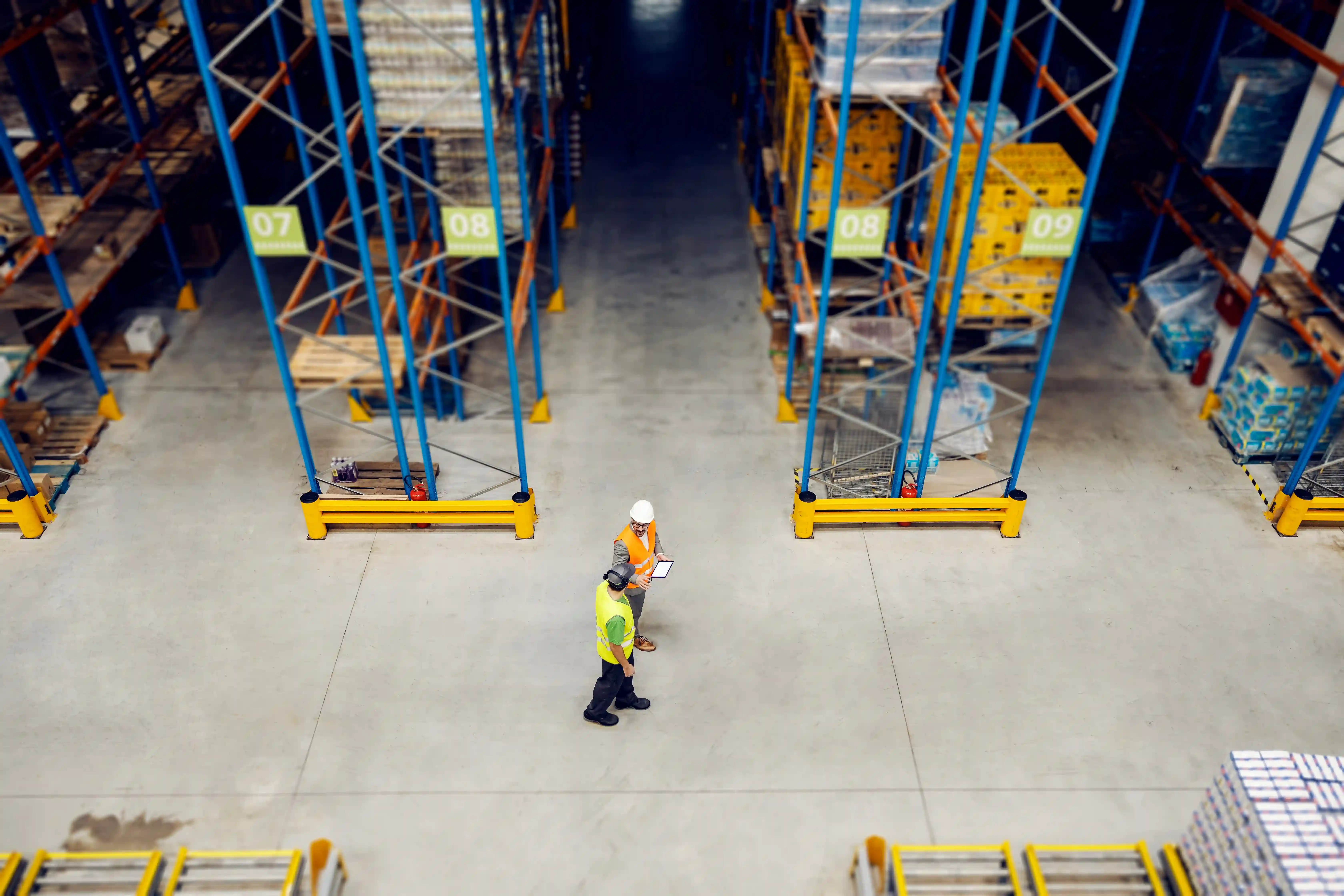 two men wearing high-vis jackets walk through a busy warehouse
