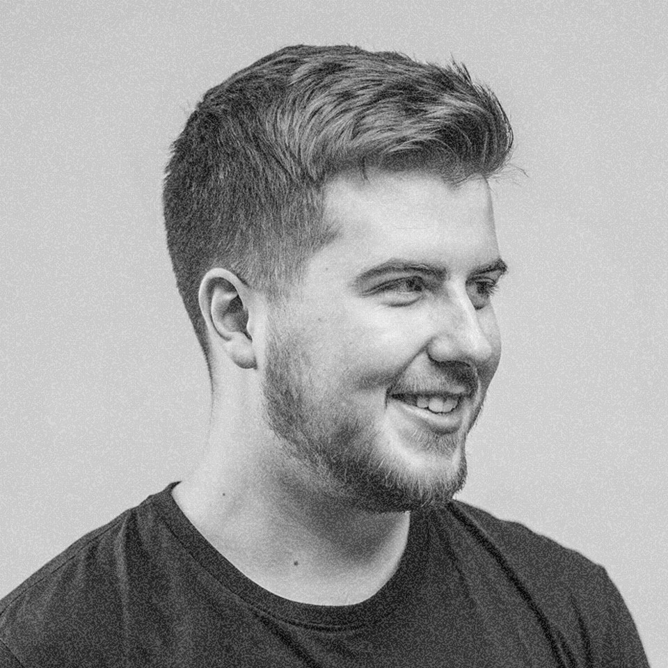 Portrait of a young man with short hair, wearing a dark t-shirt, against a plain background.
