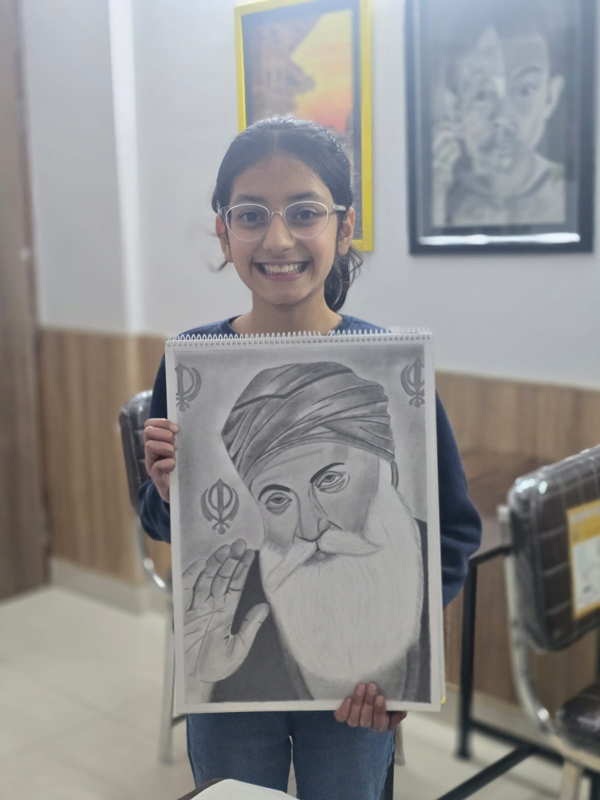 A young girl smiles while holding a black-and-white sketch of a Sikh guru in the Creative Pod studio