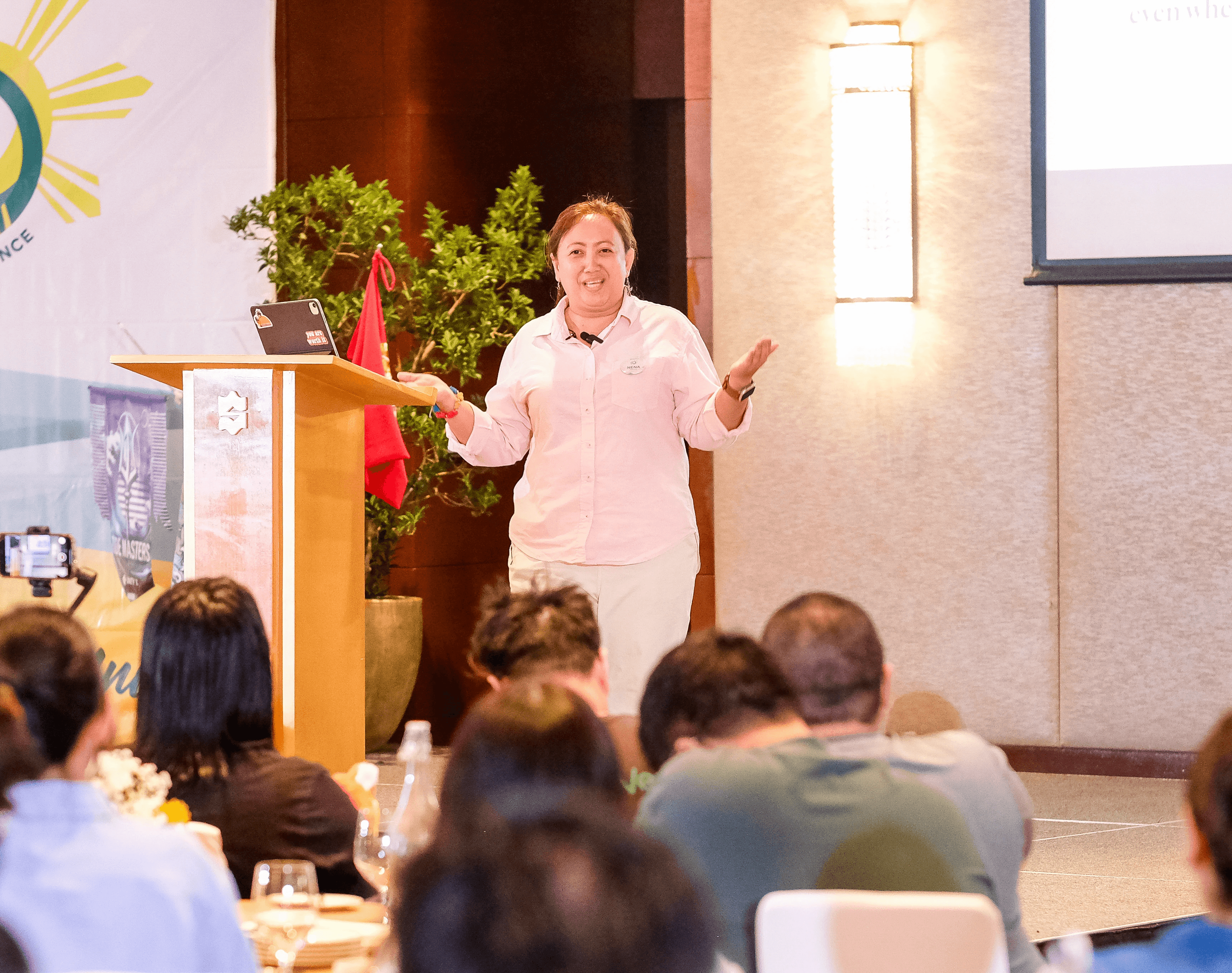 A small photo of a presenter in front of a crowd.