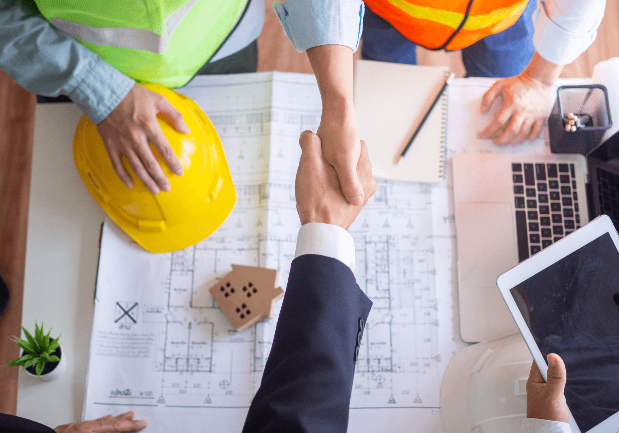 Client and contractor shaking hands over architectural blueprints, finalizing a design and build agreement.