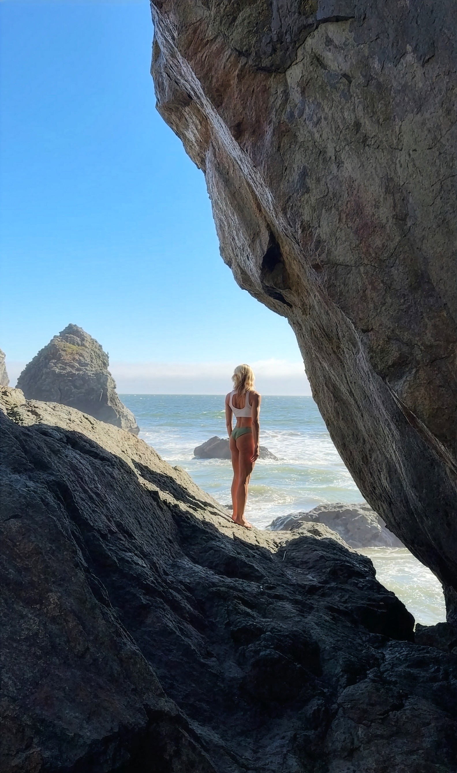 Julie Locke standing on the beach between rock formations, ocean behind her