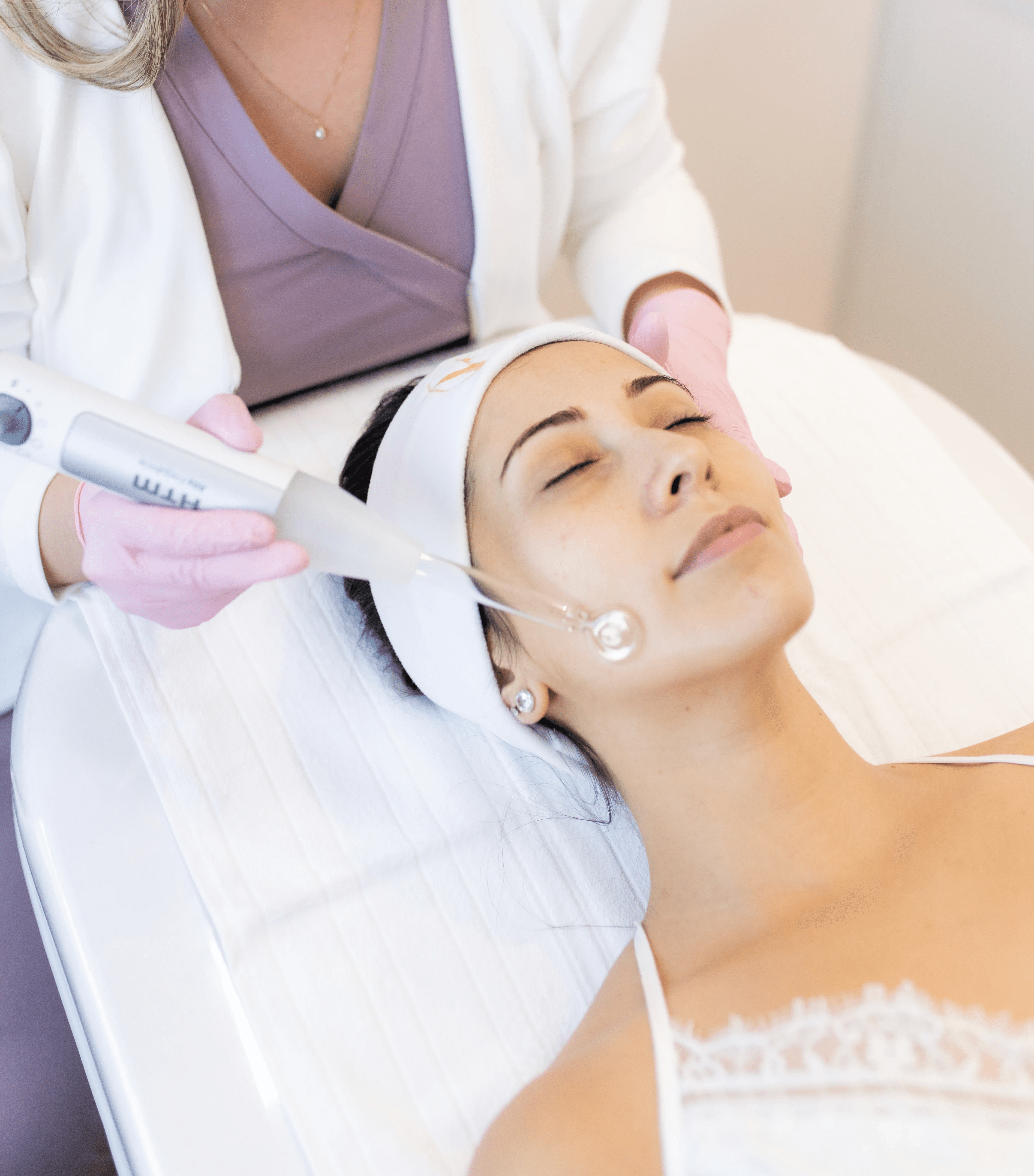 A smiling couple takes a selfie under a clear blue sky. The woman wears a red jacket, and the man, in a green top, holds a smartphone.
