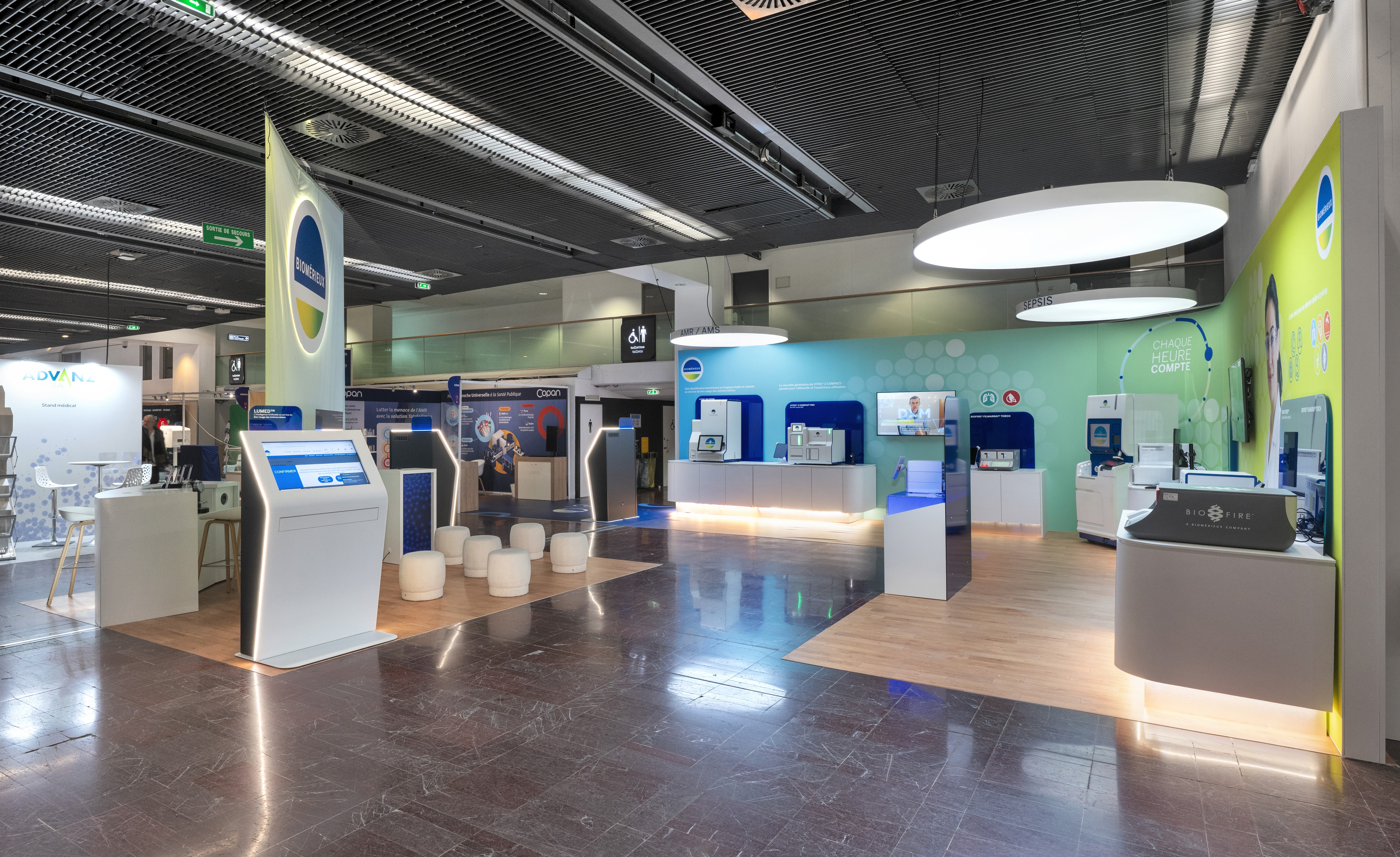 Stand bioMérieux RICAI 2025 par Expace – vue intérieure des zones AMR/AMS Sepsis et Urgences avec ilots produits rétroéclairés, écrans cliniques et grands visuels professionnels de santé