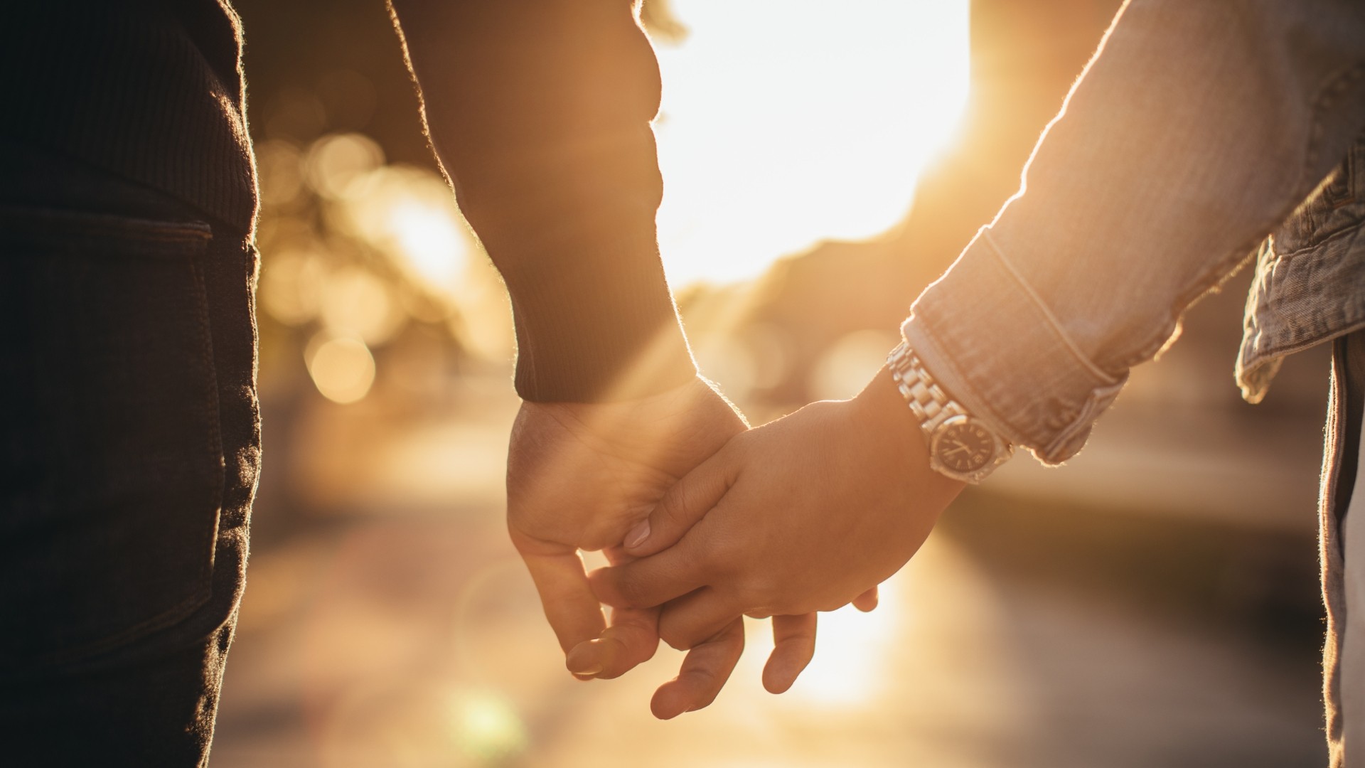 2 personen halt händchen, die sonne erhellt das bild
