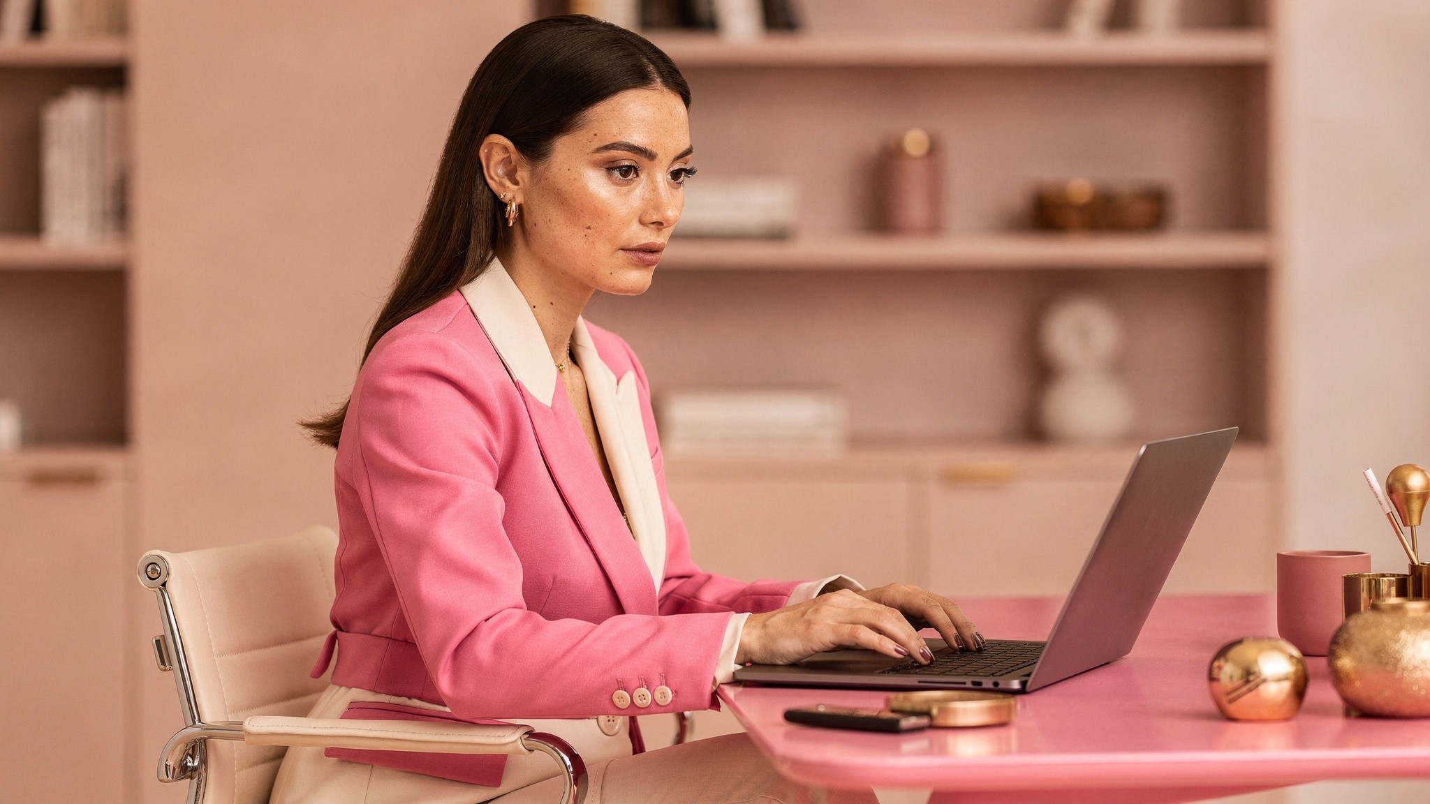 Adult creator designing carousel slides on a laptop at a styled pink desk