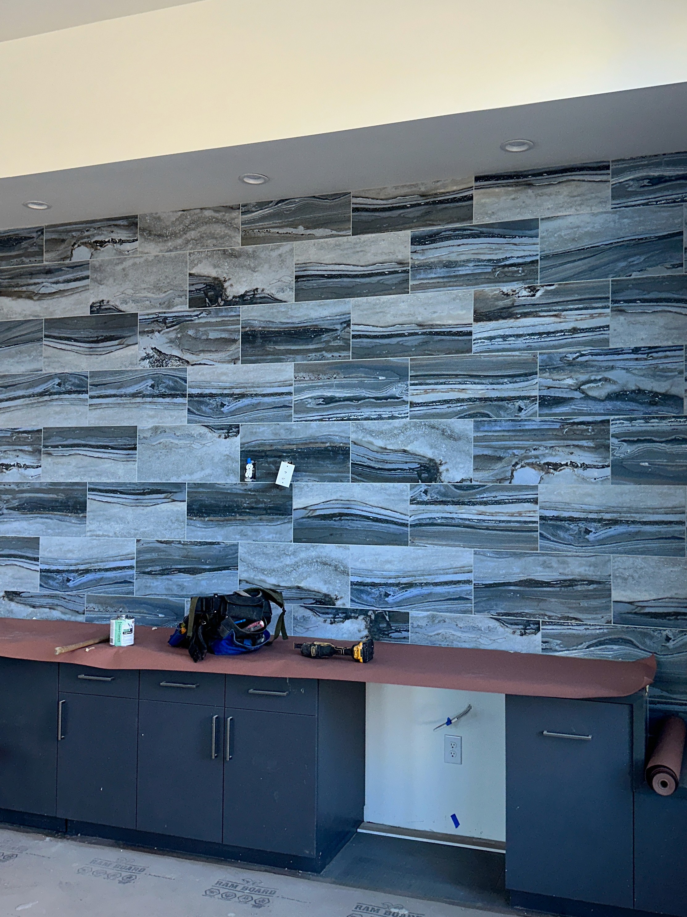 Modern wall with staggered rectangular gray and blue vein-patterned tiles installed above a built-in cabinet and counter.