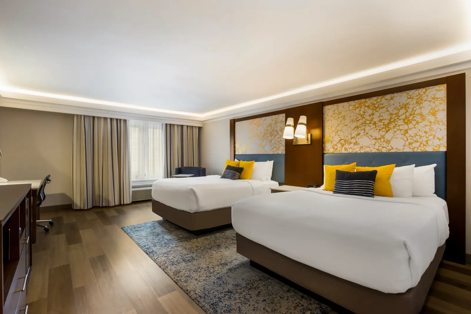 A hotel room with two beds, a desk, and a window.