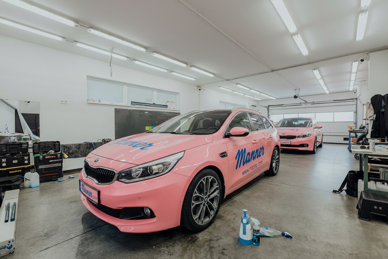 Két élénk rózsaszínre fóliázott, Manner logóval ellátott Kia céges autó a Nortek budapesti műhelyében. Figyelemfelkeltő, prémium minőségű flottadekor és flottadesign kivitelezés a tökéletes márkaépítés jegyében.