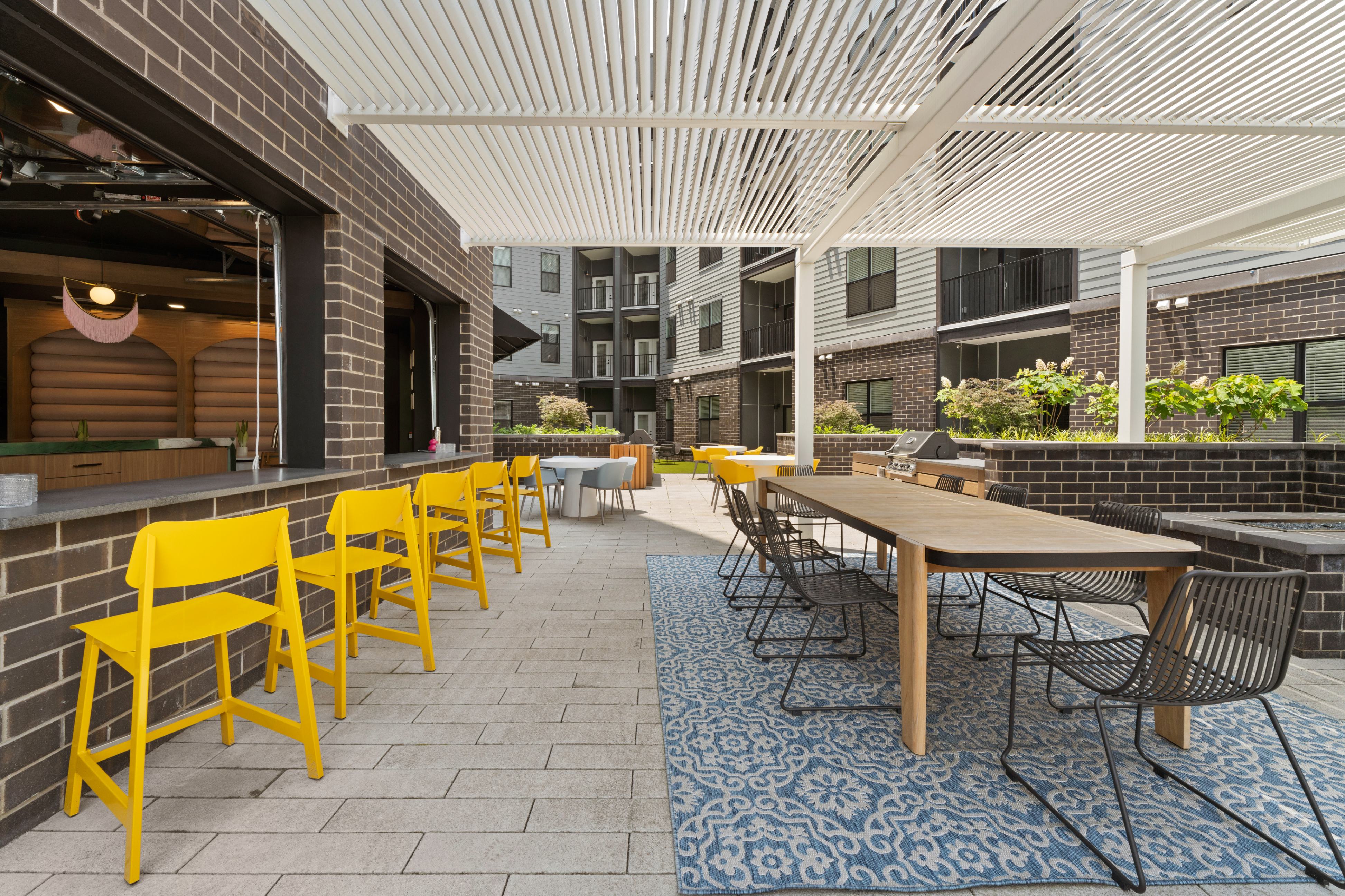 Patio at the park featuring a grill and garage windows, surrounded by greenery and outdoor seating.