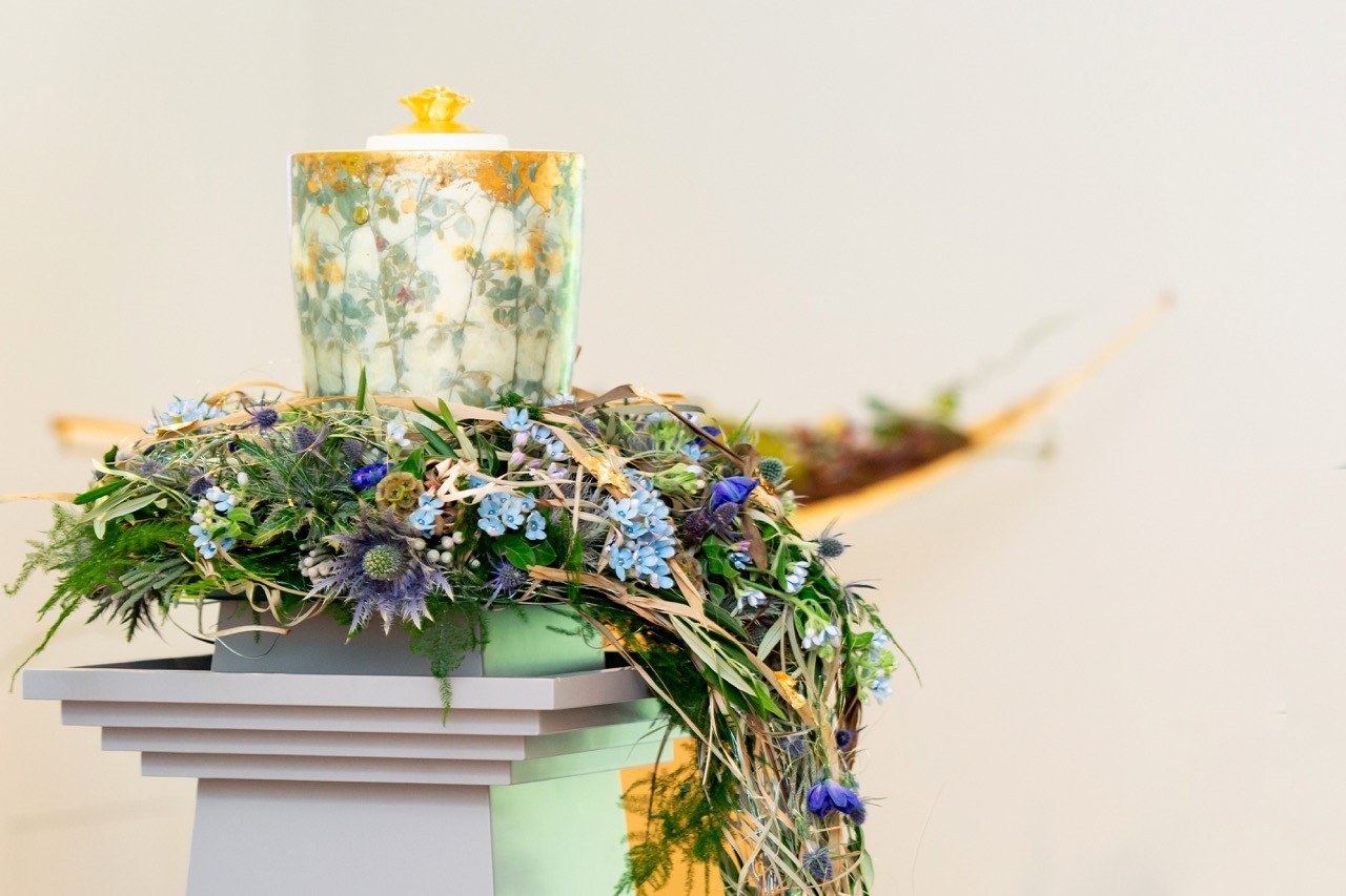 Gestaltete Urne mit Blumenschmuck auf einem Podest