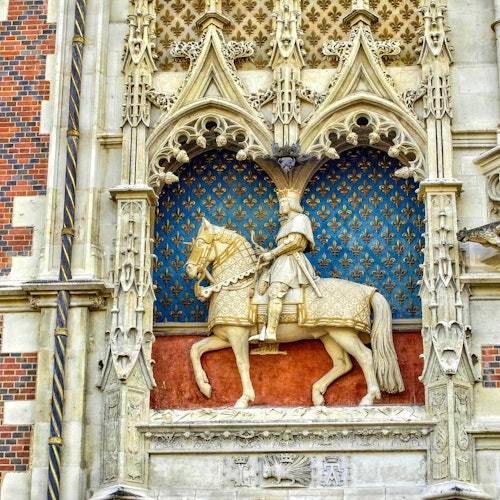 Statue en pierre ornée d'un homme à cheval, placée dans une niche de style gothique avec des détails complexes, sur un fond bleu à motifs.