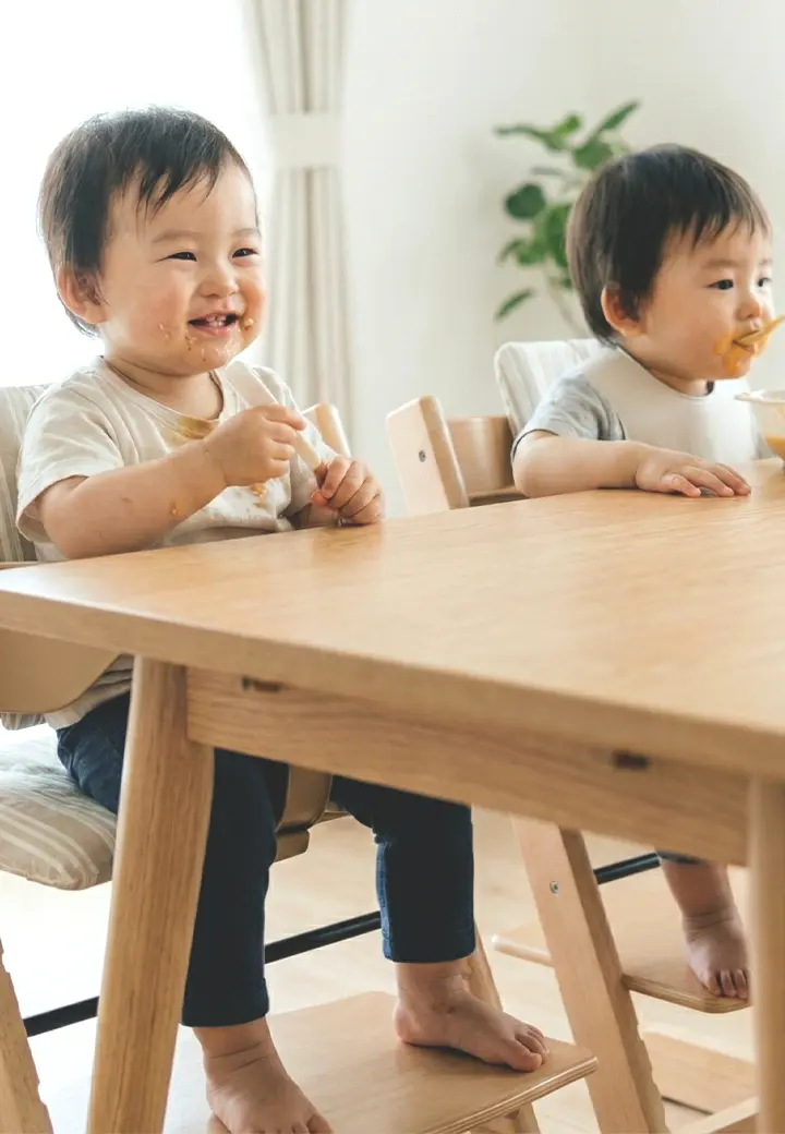 two asian toddlers eating on dinner table
