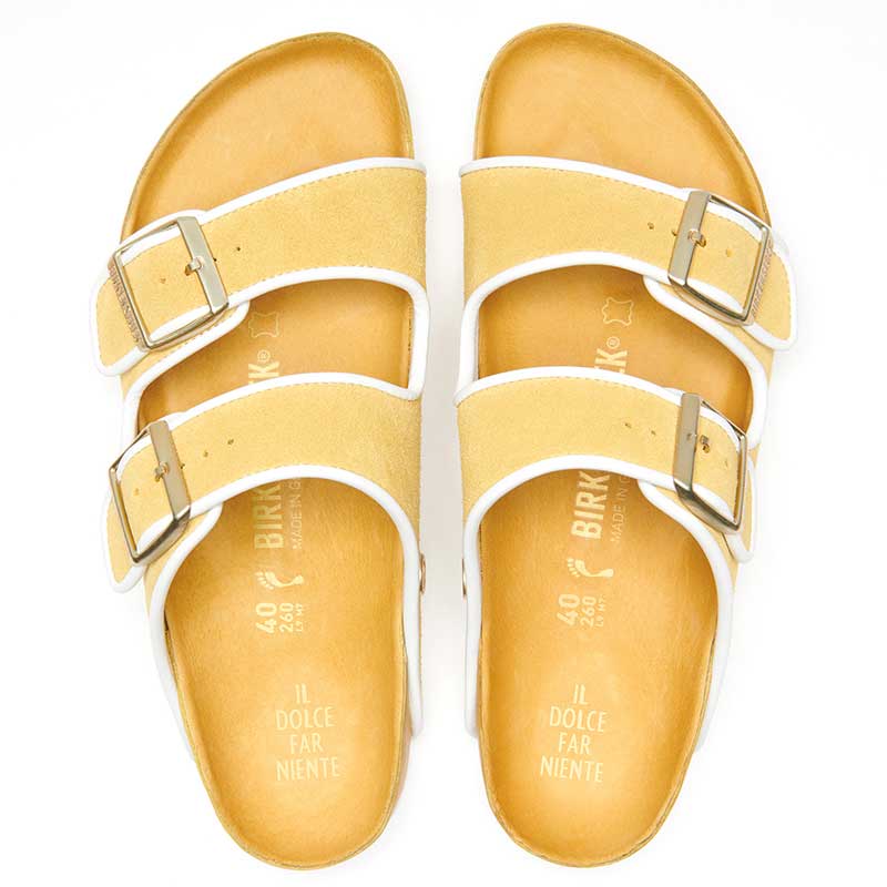 Yellow suede Arizona sandals with white trim — elegantly presented over a chic, patterned background.