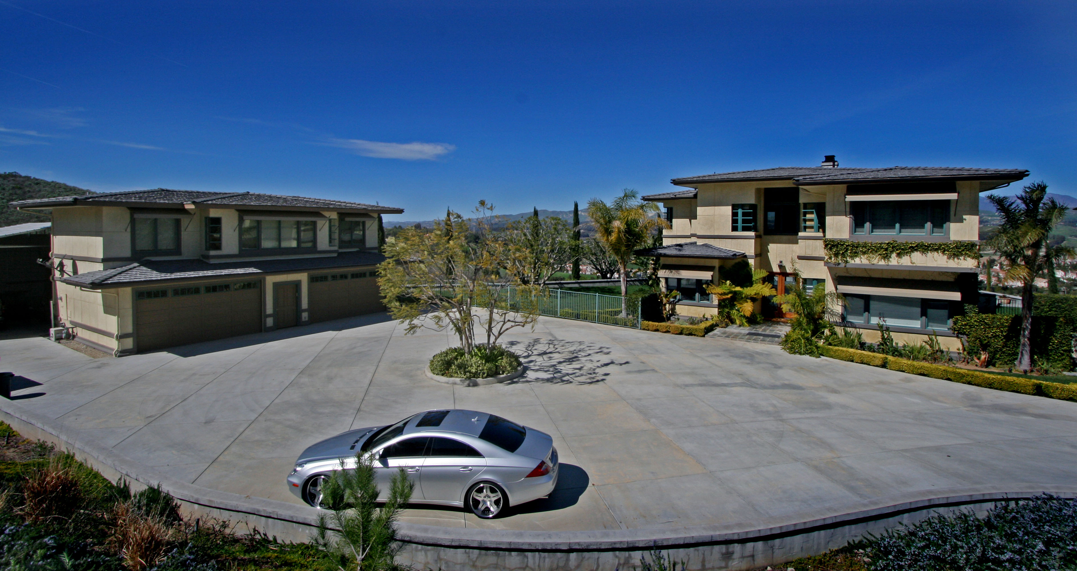 Aerial view with a blue sky, showing two buildings and a car in the foreground, emphasizing the home’s placement in its surroundings.