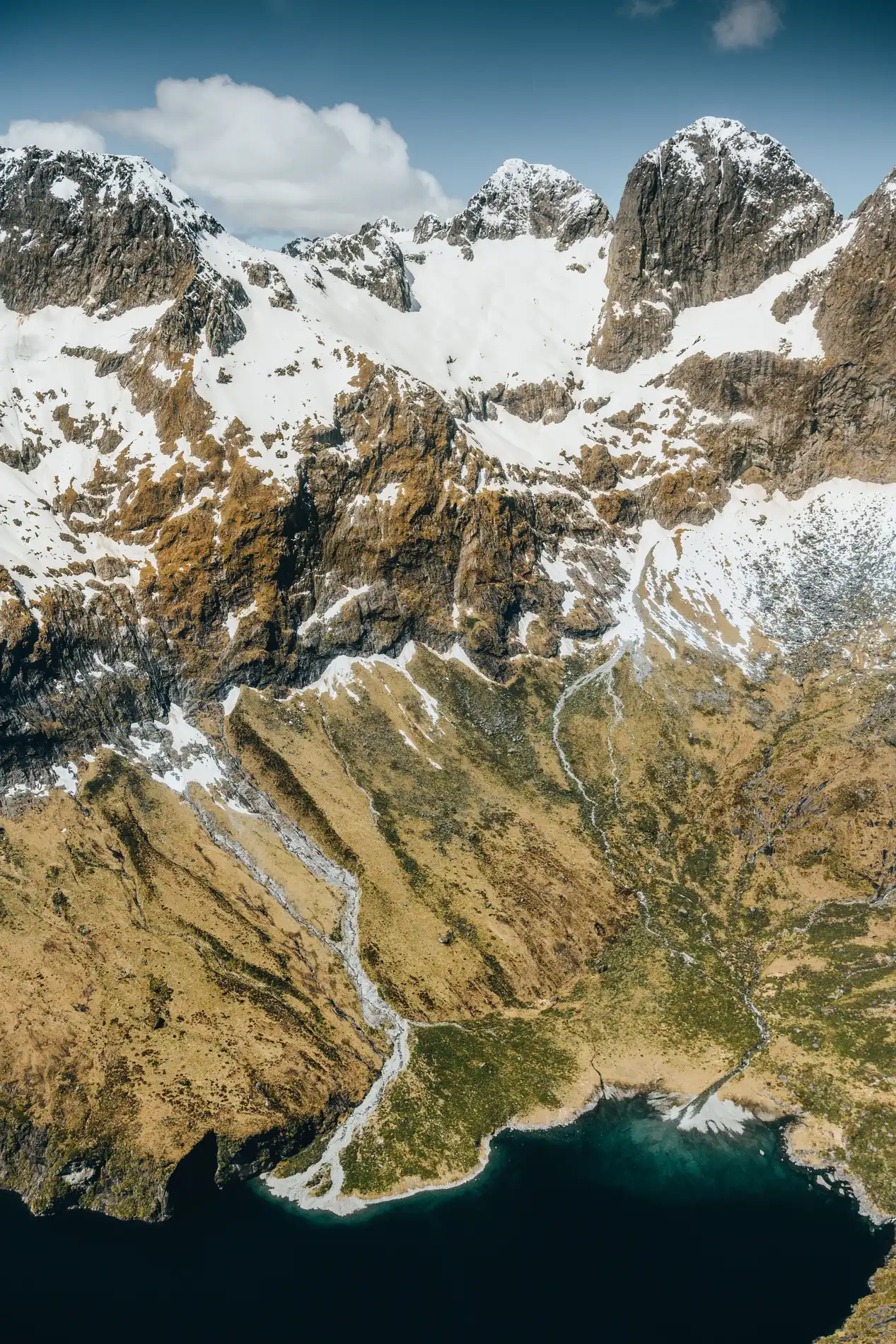 Aerial of snow-covered peaks falling away to a dark alpine lake