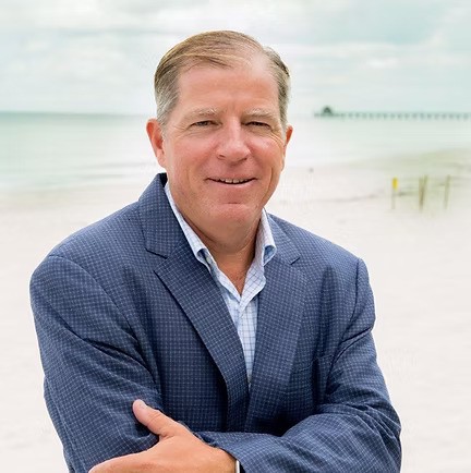 a man in a suit standing in front of a white sand beach