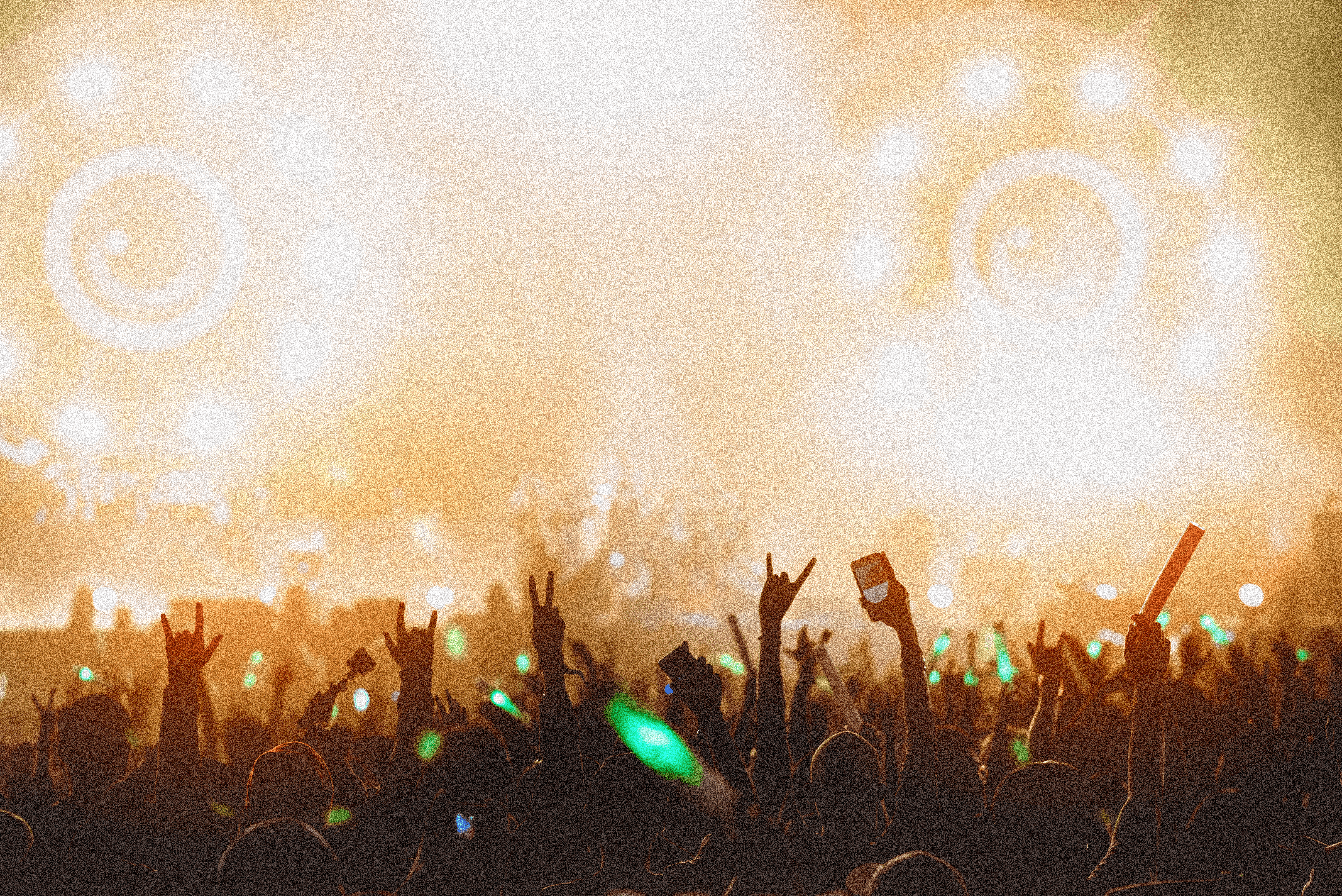 A grainy image showing a bright stage at a festival with the sillouettes of hands and phones in the crowd visibile