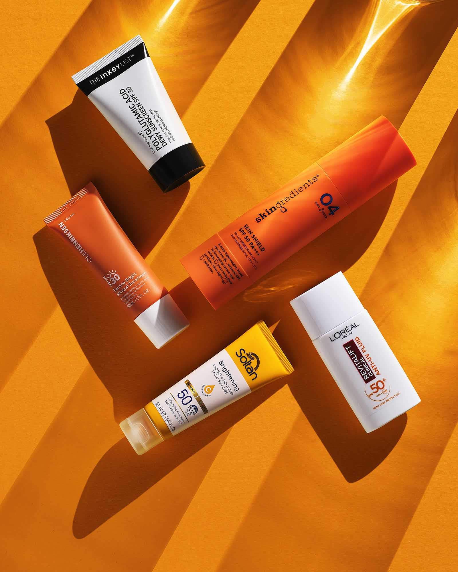 Four skincare products are arranged on an orange backdrop, showcasing various colors and packaging designs.