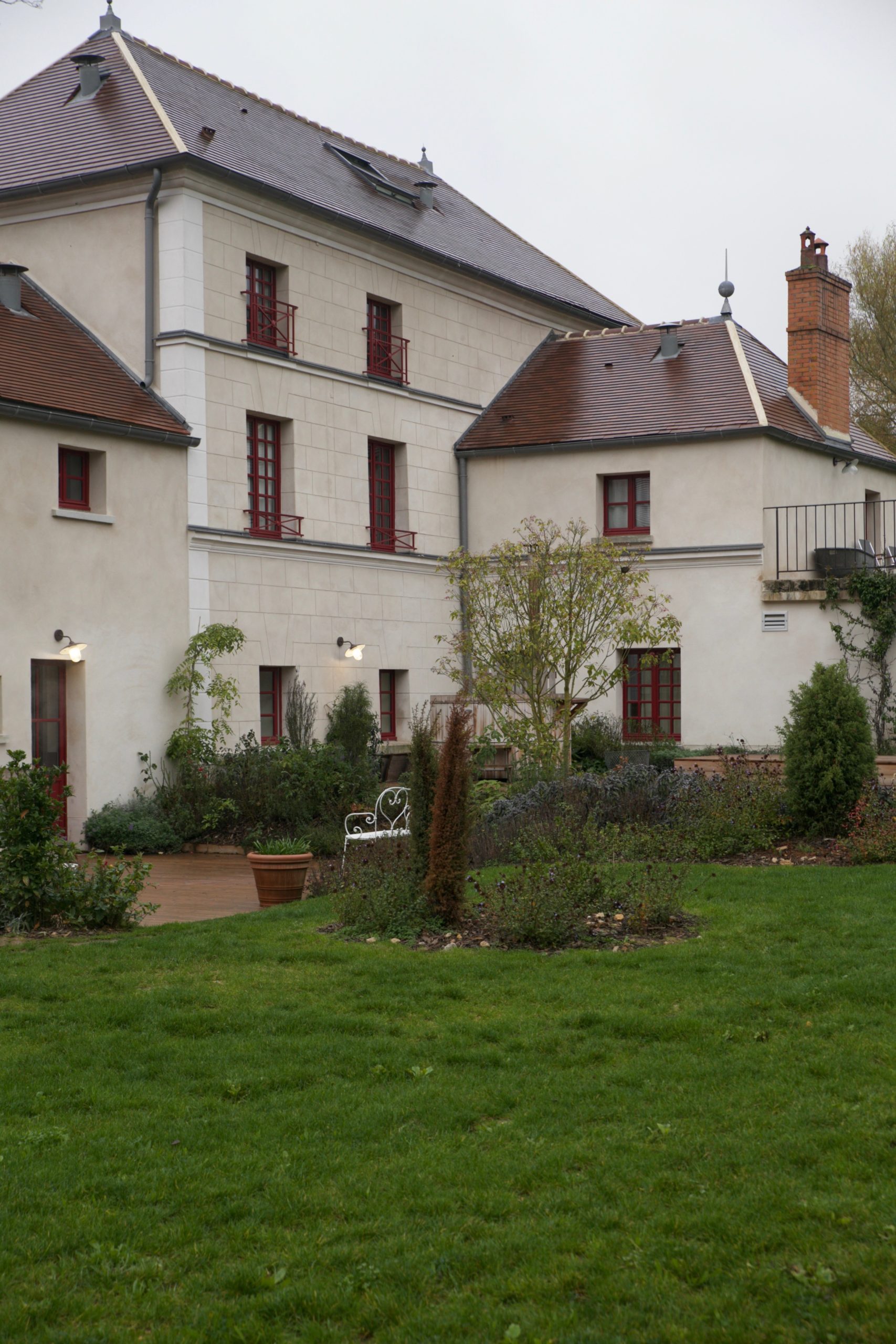 Stone manor house exterior with red-framed windows, a tiled roof and a garden lawn