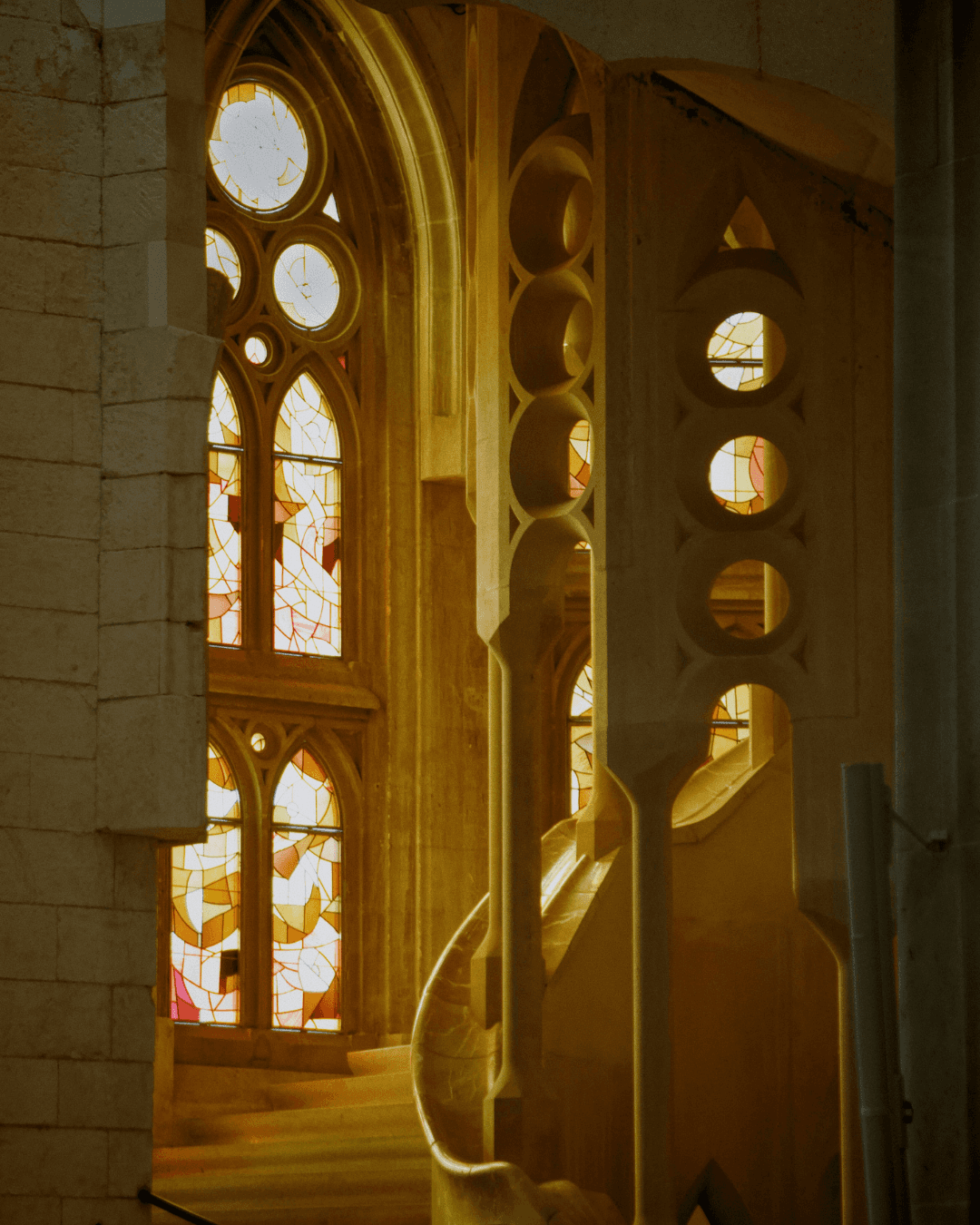 Interior staircase of the Sagrada Família bathed in warm golden light from stained glass windows.