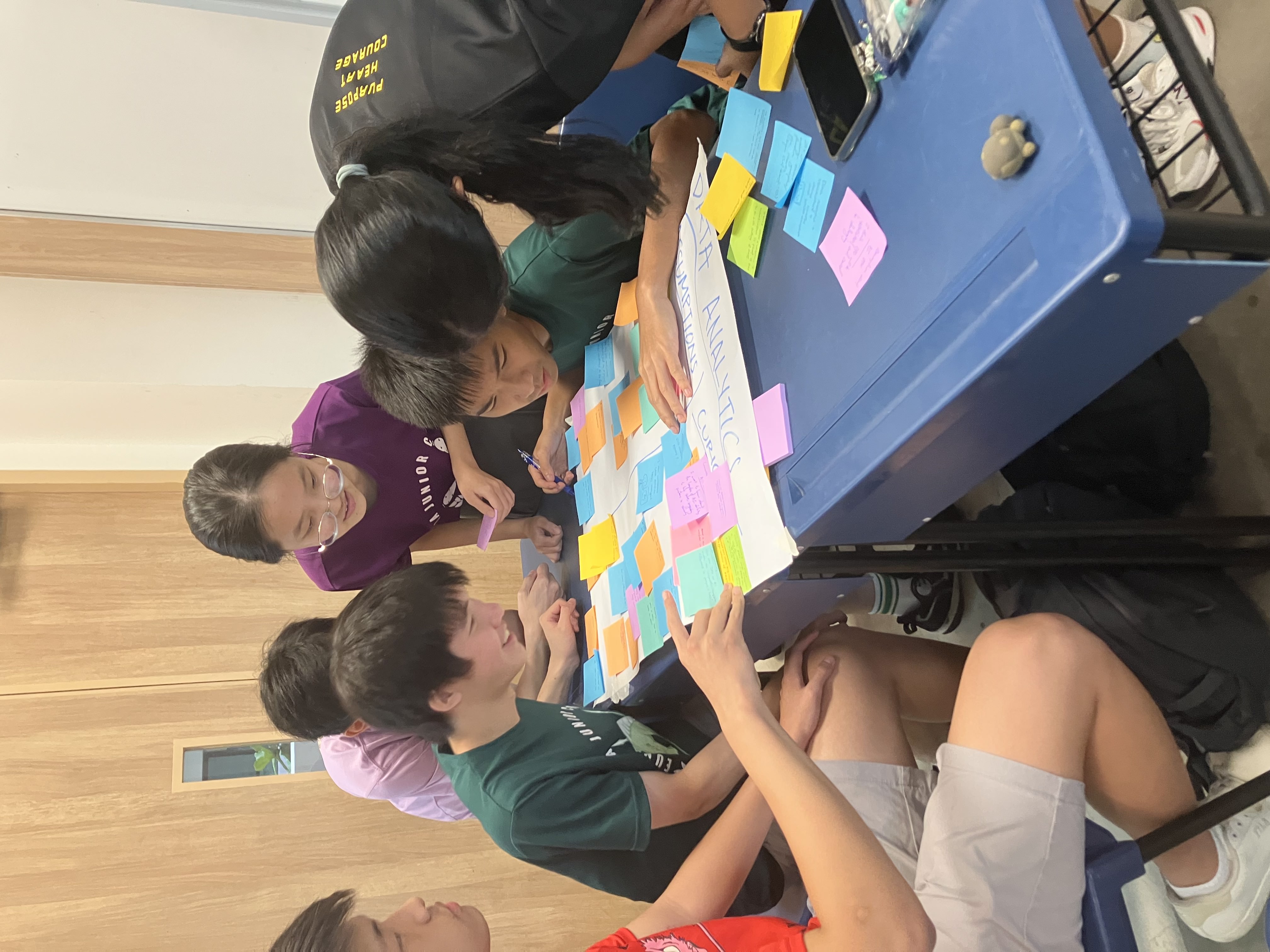 A smiling young man with crossed arms, wearing a plaid shirt and white t-shirt, poses against a dark background.